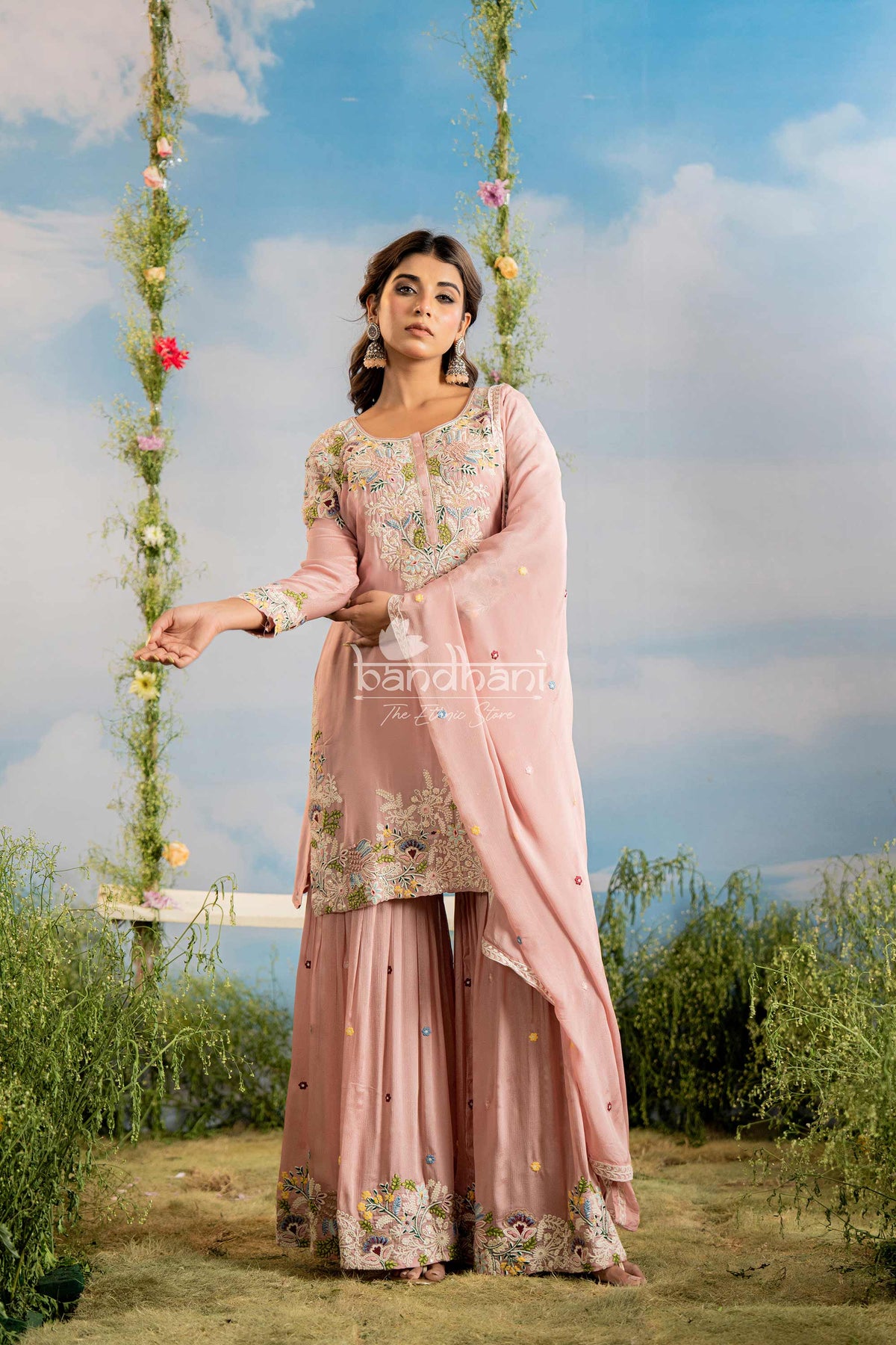 Woman in a pink traditional outfit standing on a grassy field with a floral swing in the background.