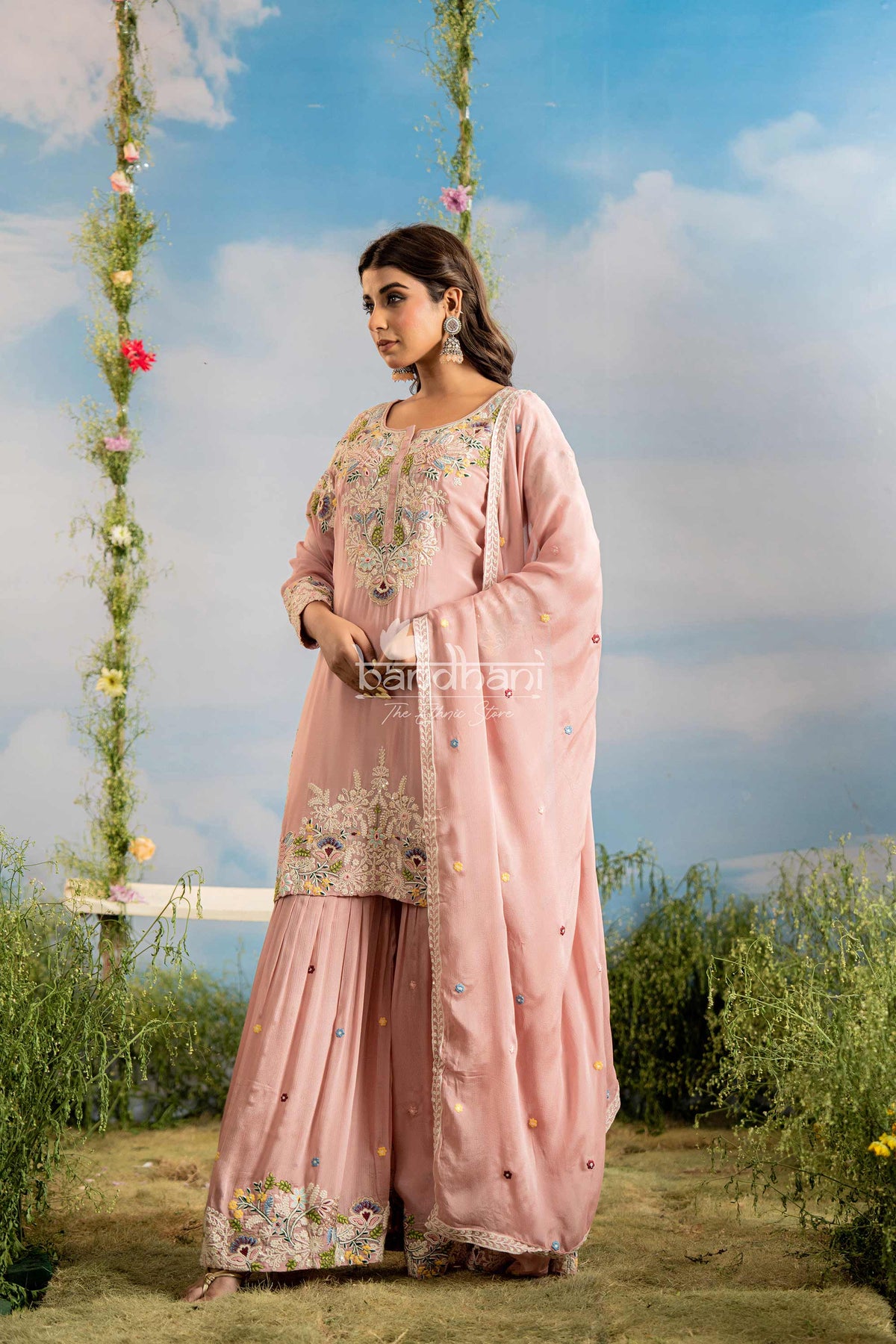 Woman in a pink traditional outfit with floral patterns standing outdoors against a scenic background.