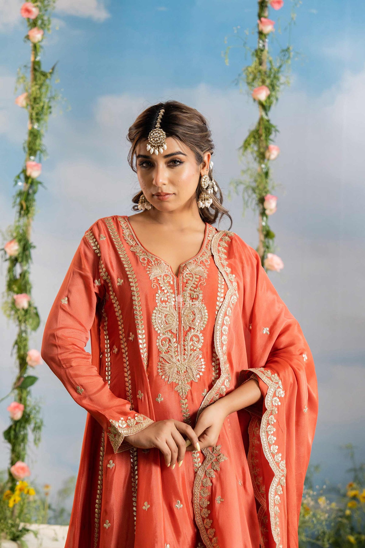 Woman in an orange traditional outfit with floral decorations in the background