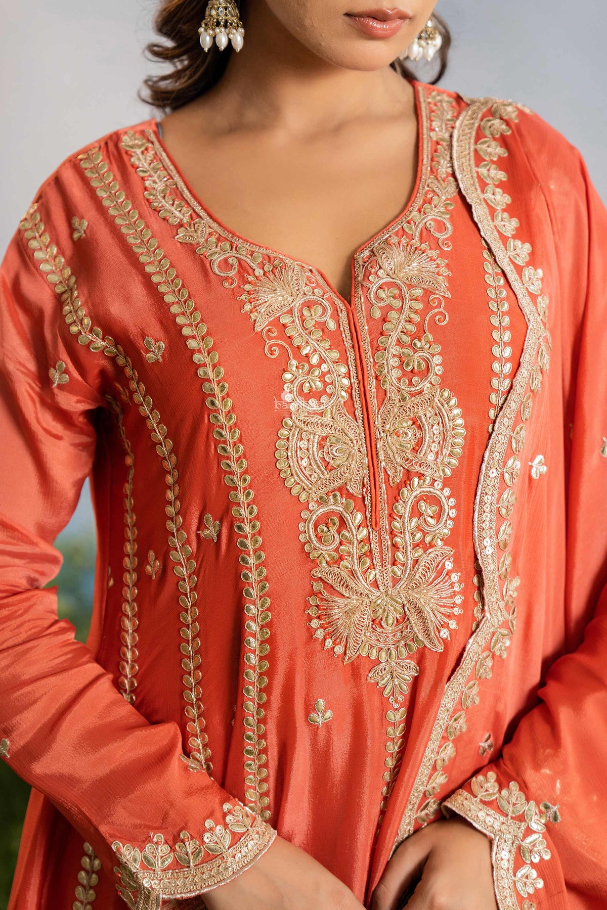 Coral pink traditional outfit with intricate gold embroidery on a blurred background