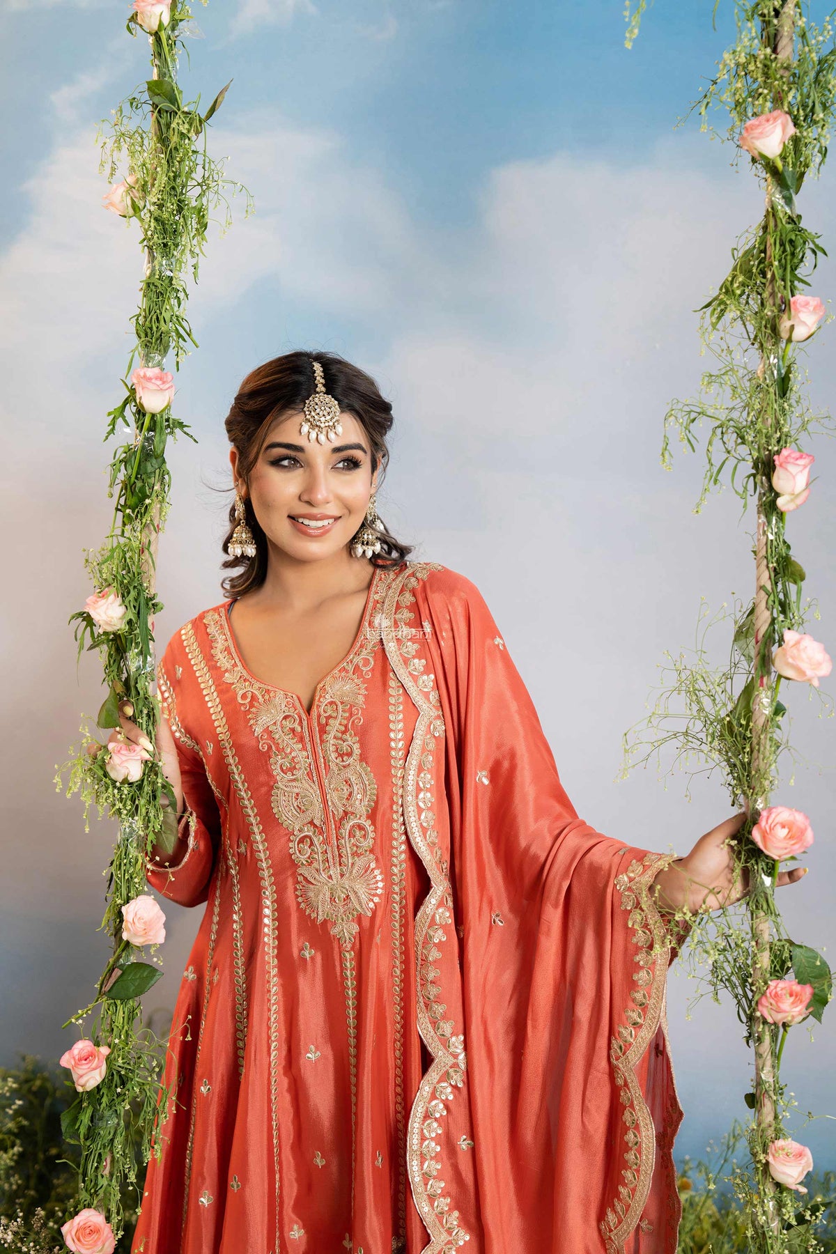 Woman in a coral traditional outfit with floral decorations against a blue sky.