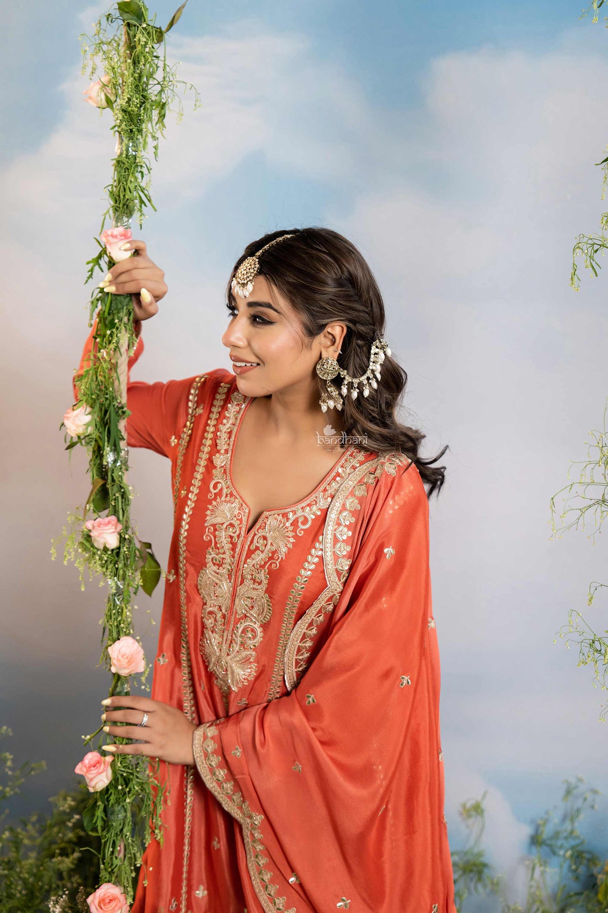 Woman in traditional orange outfit with floral decorations against a natural background