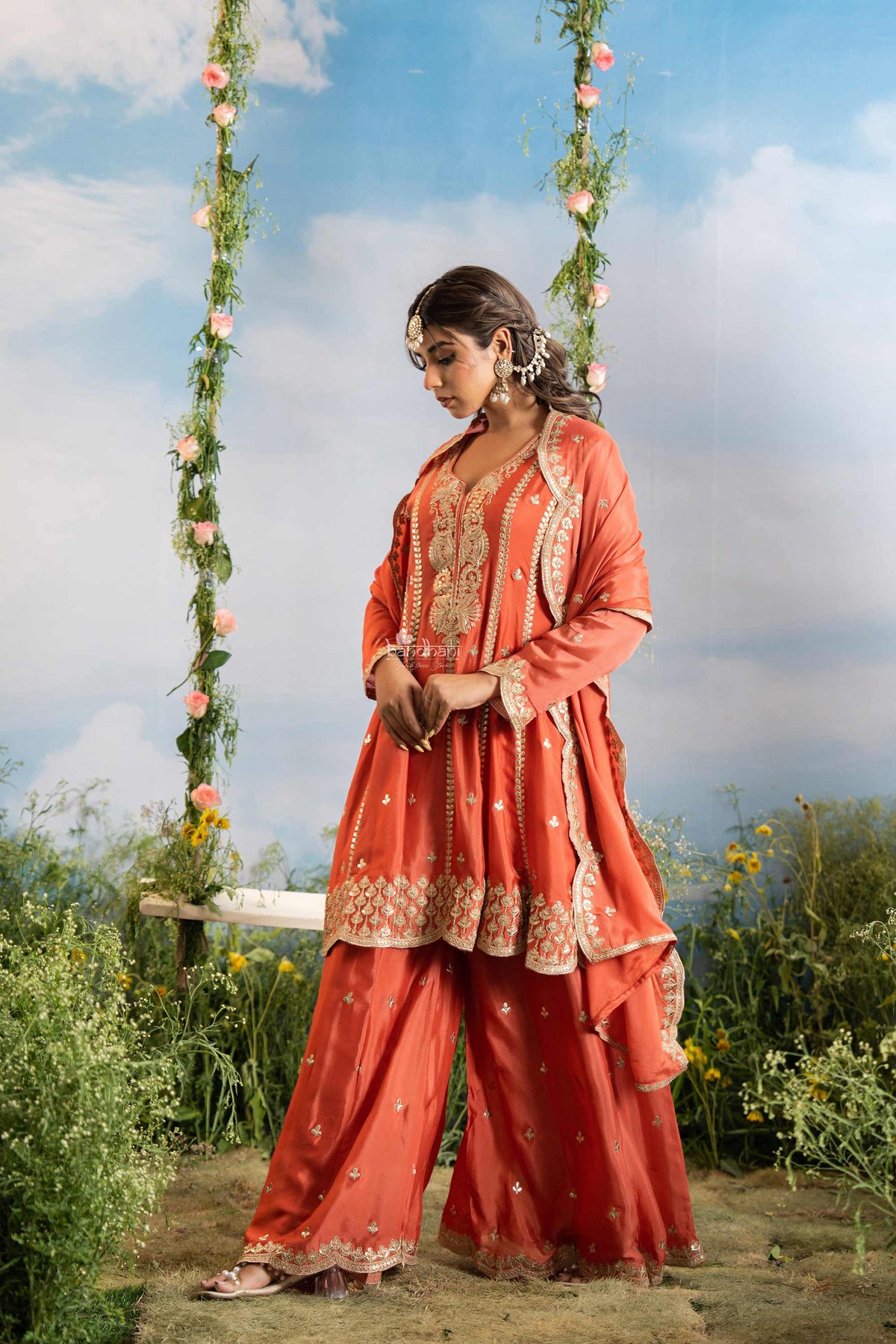 Woman in traditional coral outfit with floral decorations against a natural background