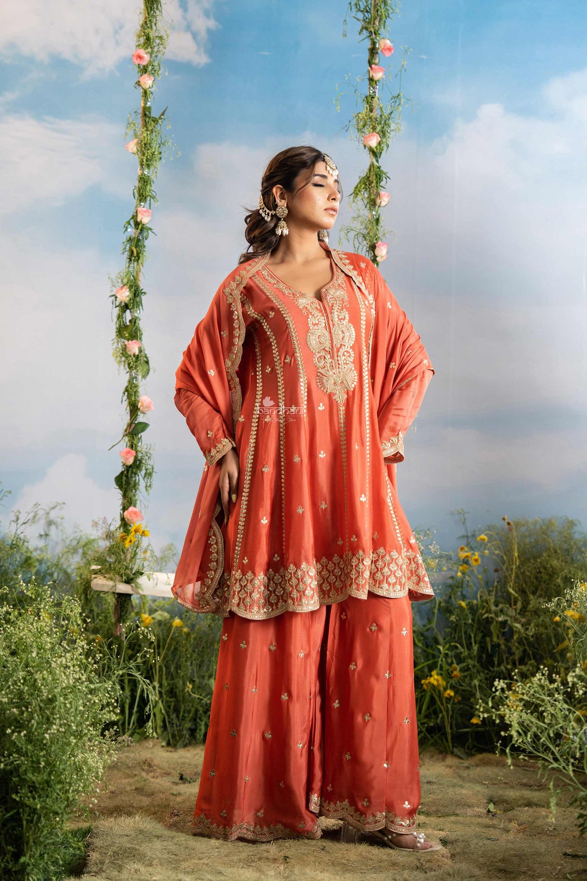 Woman in traditional coral outfit with floral decorations against a natural background