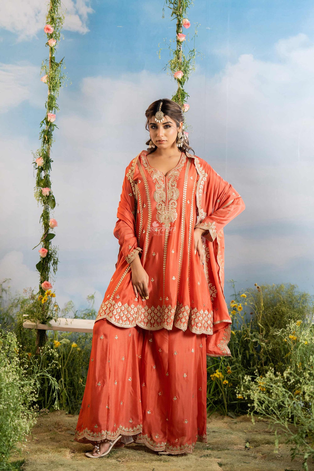 Woman in a traditional orange outfit with floral decorations against a natural background