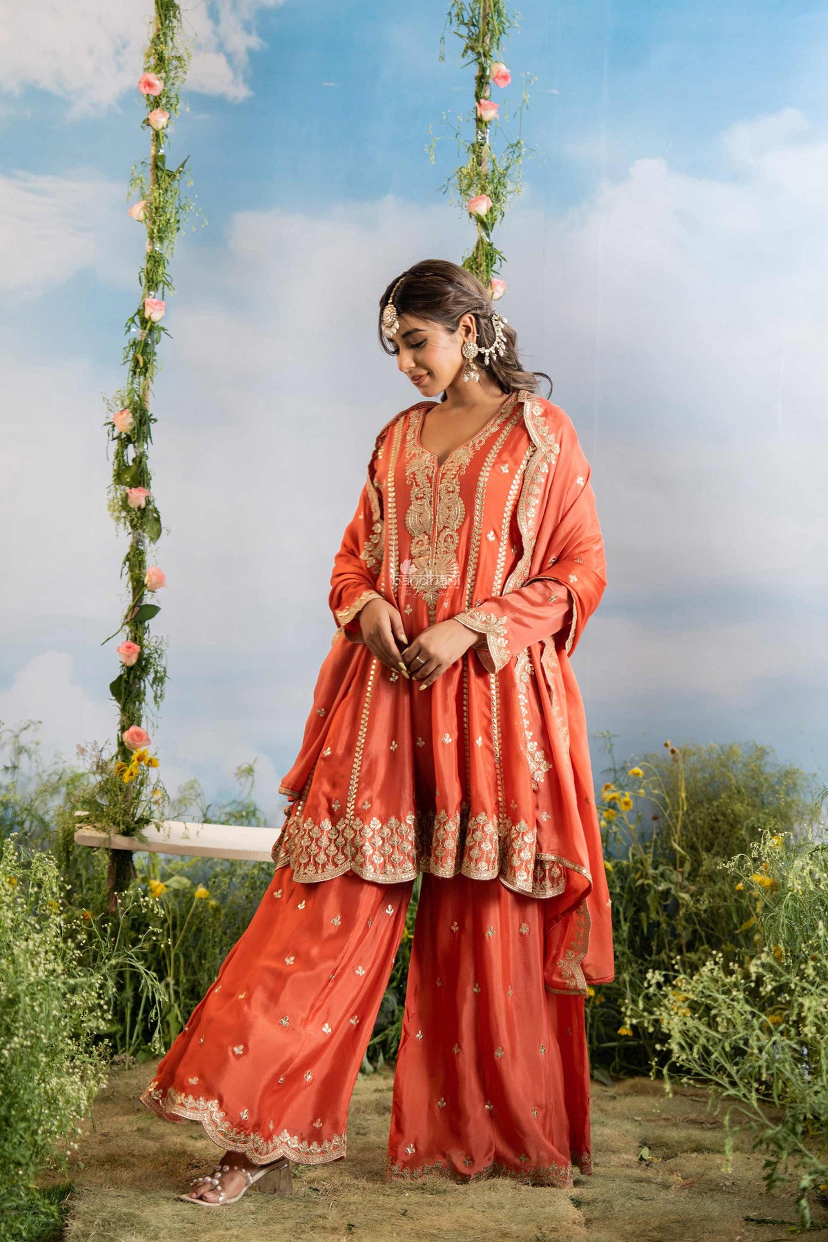 Woman in traditional coral outfit with floral decorations against a natural background
