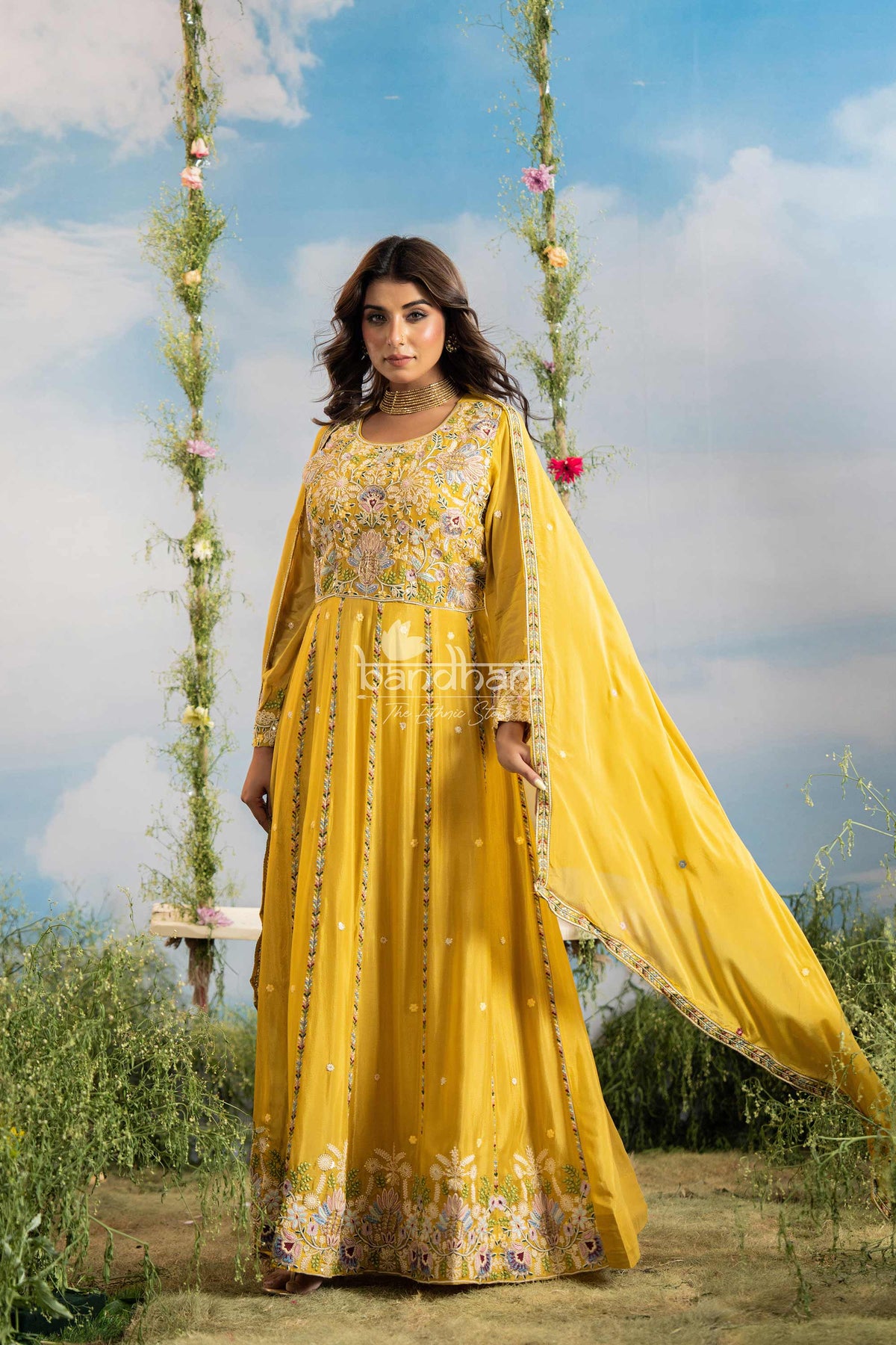 Woman in a yellow traditional outfit standing outdoors with greenery and blue sky in the background
