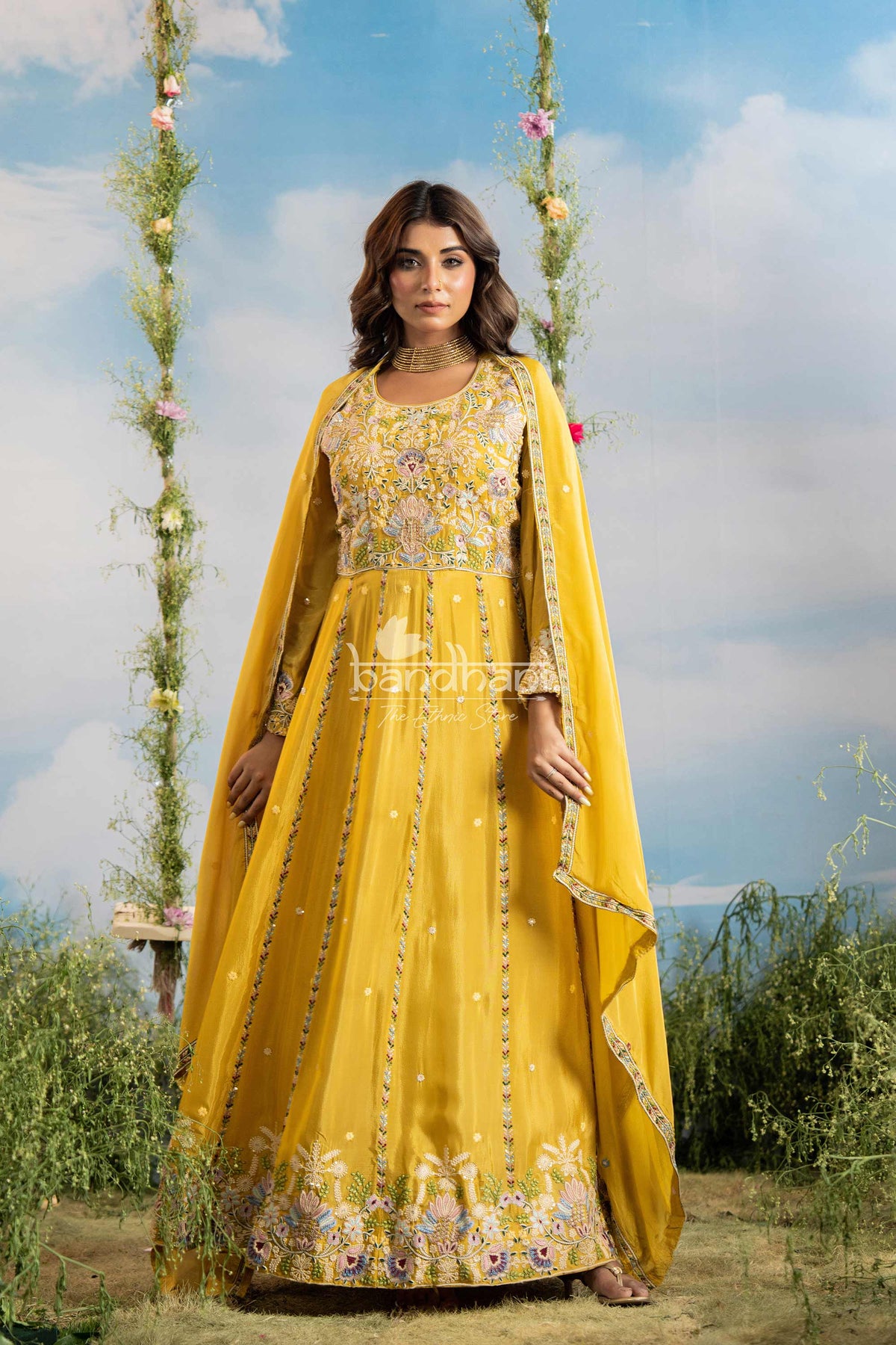 Woman in a yellow traditional outfit with floral patterns standing outdoors against a blue sky.