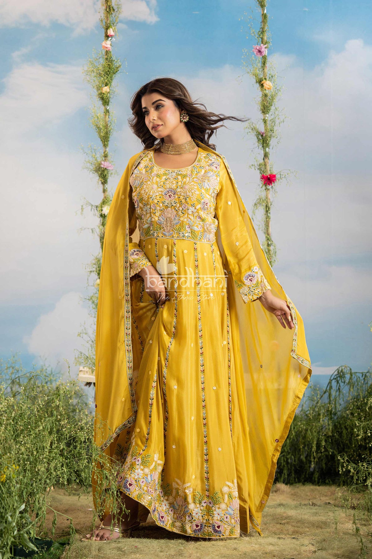 Woman in a yellow traditional outfit with floral patterns standing outdoors against a blue sky.