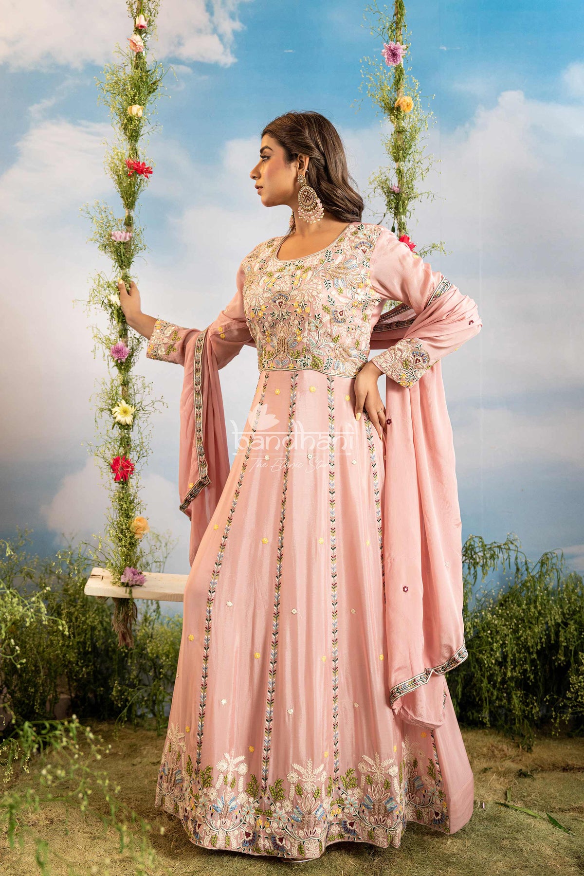 Woman in a pink traditional outfit standing outdoors with a floral swing in the background
