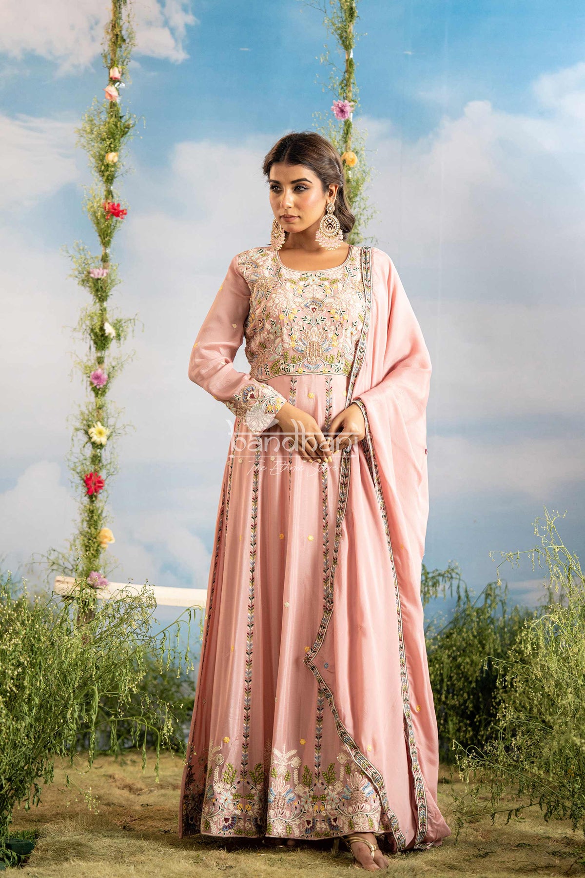 Woman in a pink traditional outfit with floral patterns standing outdoors against a scenic background.