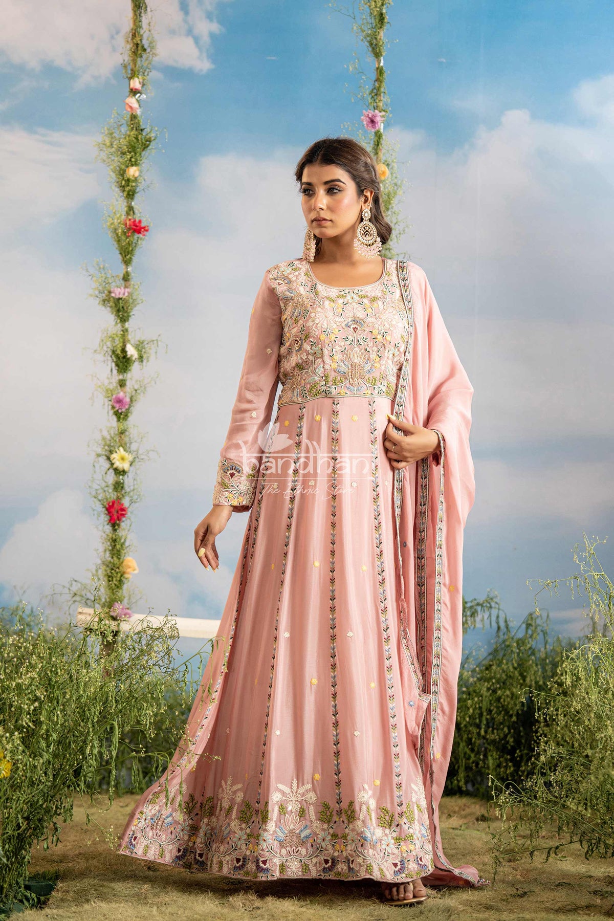 Woman in a traditional pink outfit with floral patterns standing outdoors against a blue sky.