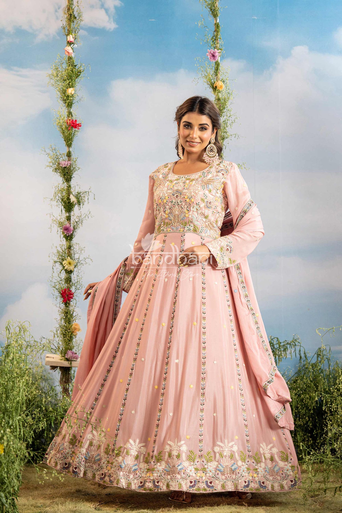 Woman in a pink traditional outfit standing outdoors with a floral swing and blue sky background