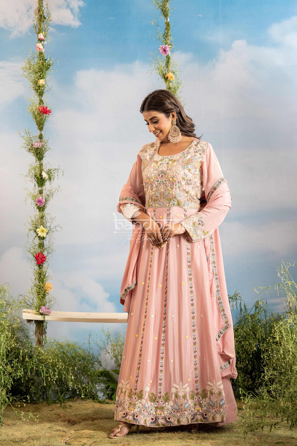 Woman in a pink traditional outfit with floral patterns standing outdoors against a blue sky.