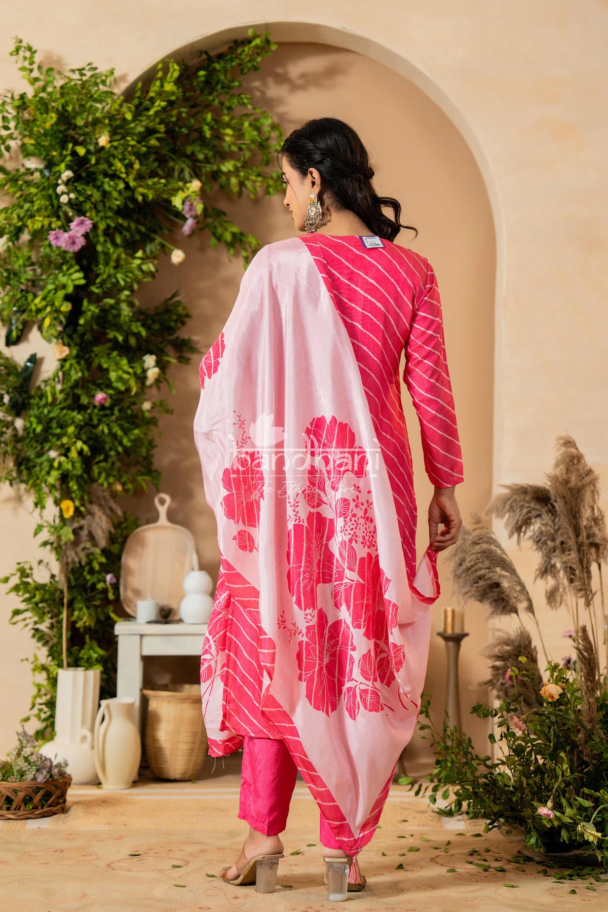 Woman in a pink and white traditional outfit standing in a decorated outdoor setting.