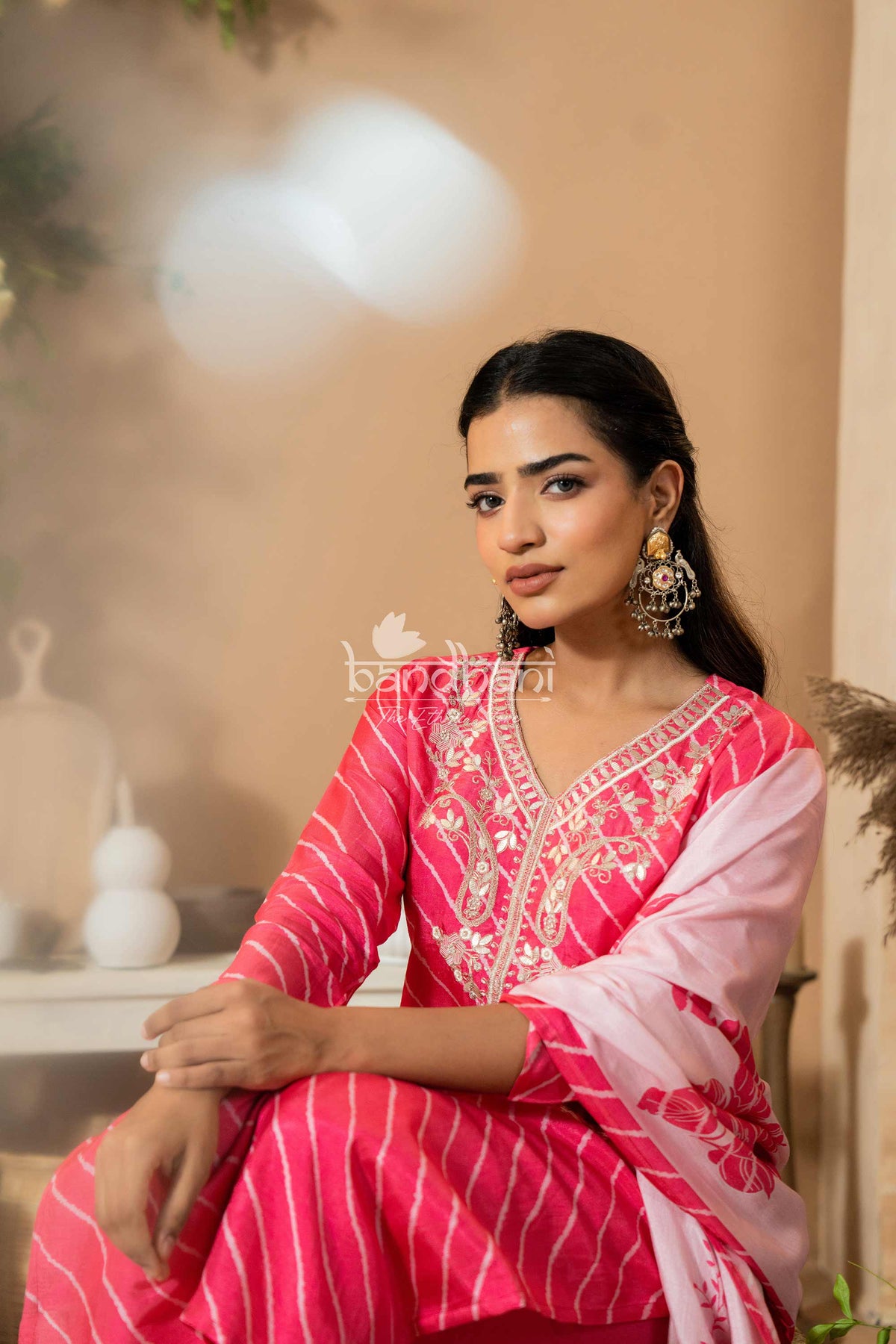 Woman in a pink traditional outfit with white embroidery sitting indoors.