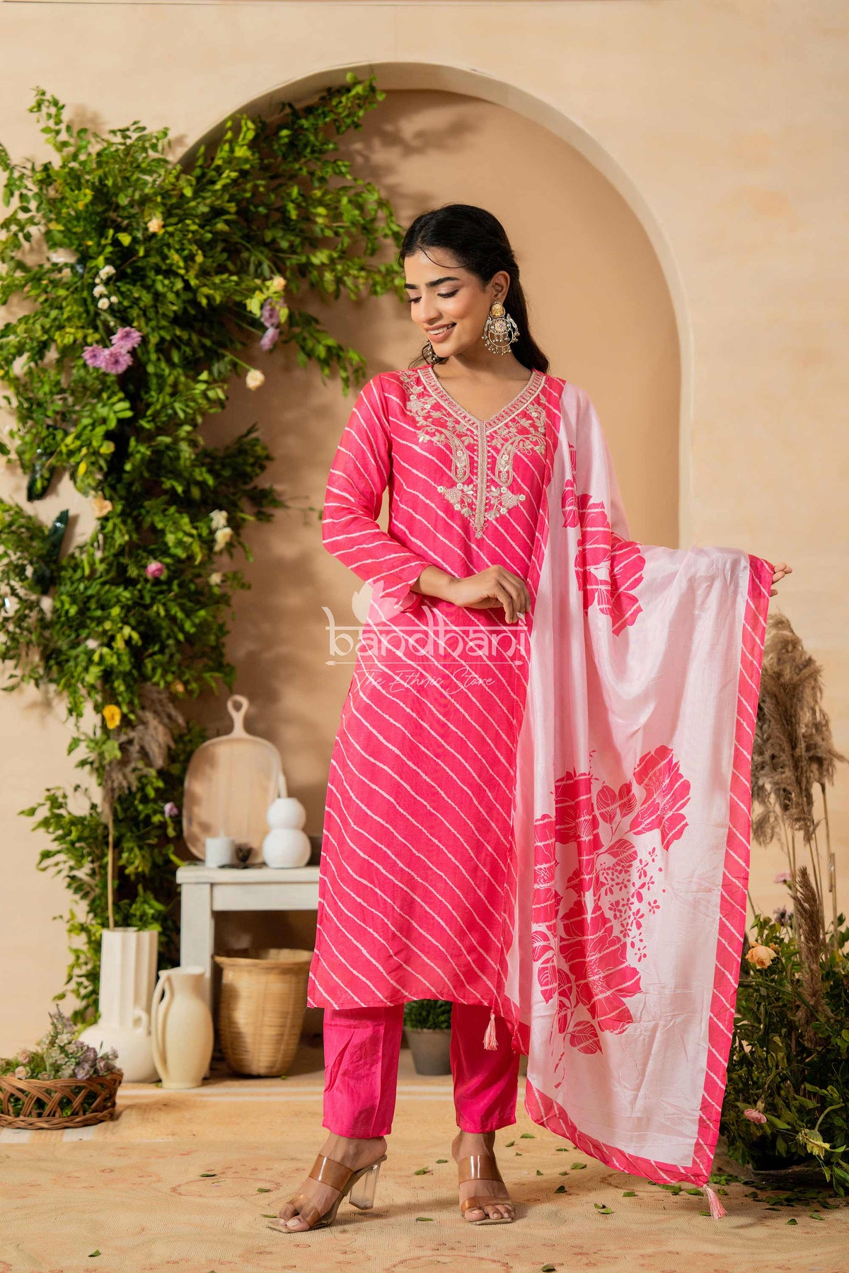 Woman in a pink traditional outfit with a white dupatta, standing in a decorated outdoor setting.