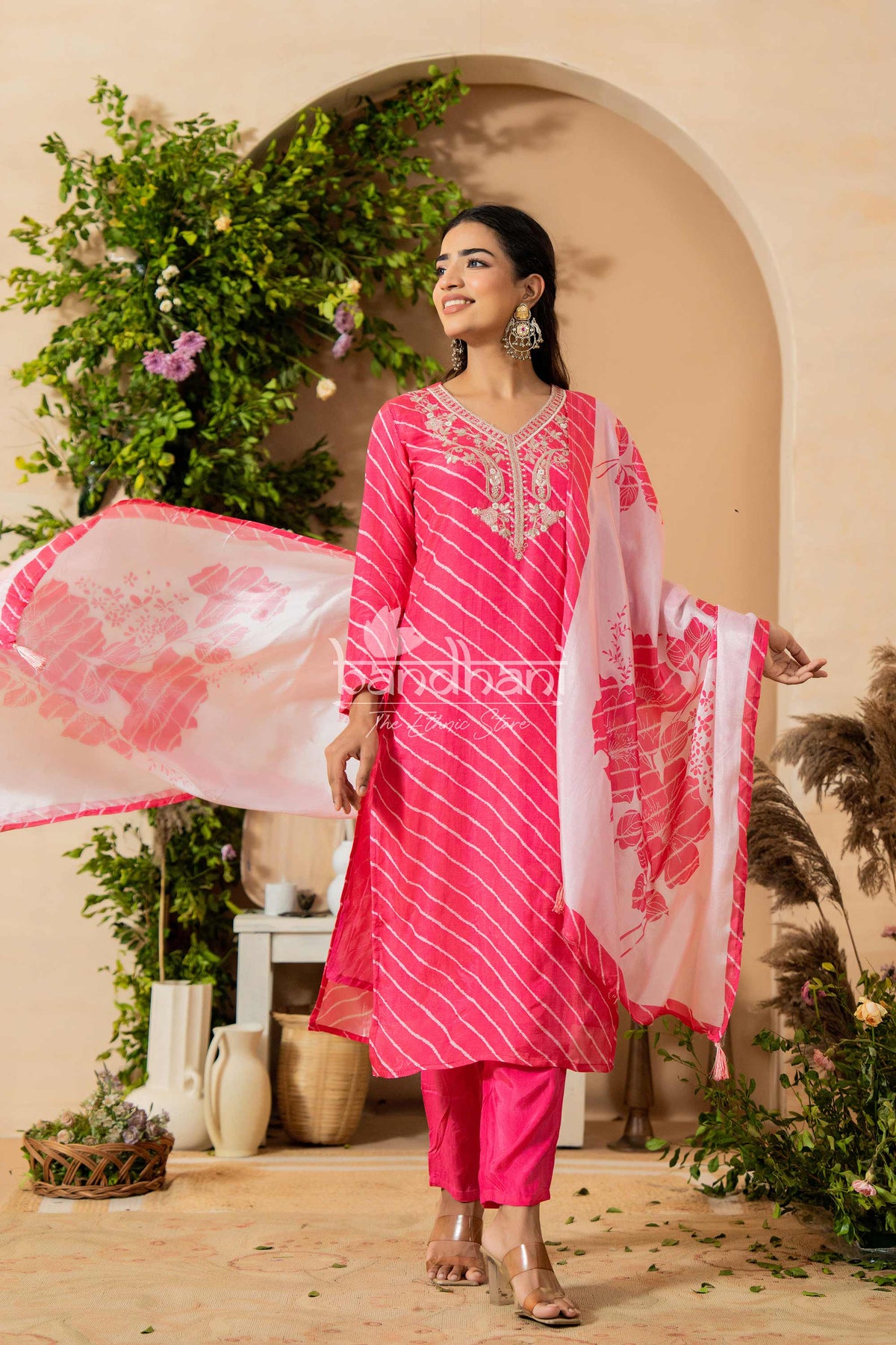 Woman in a pink traditional outfit with a matching dupatta, standing in a decorated indoor setting.