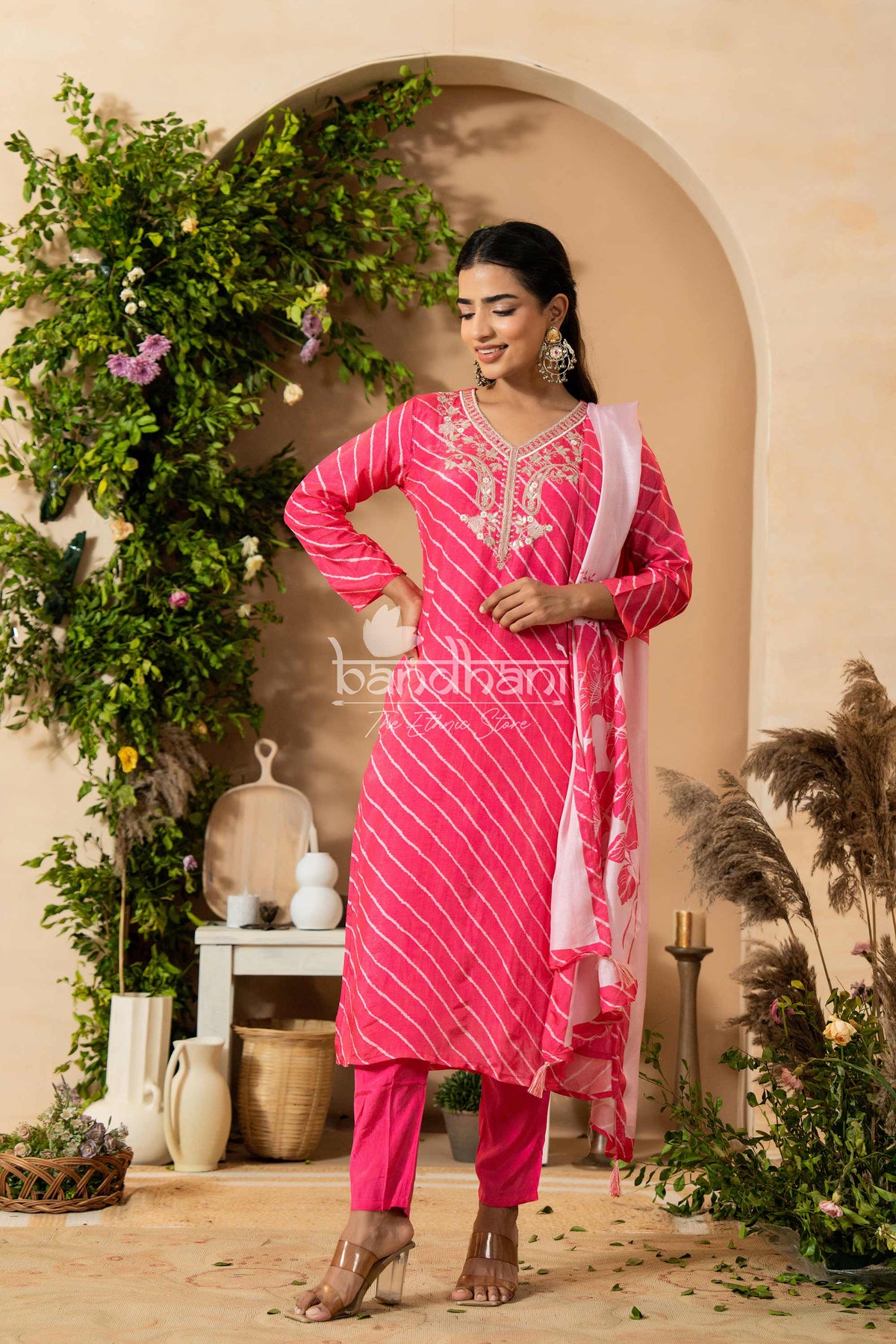 Woman in a pink traditional outfit standing in a decorated indoor setting with plants and decor.