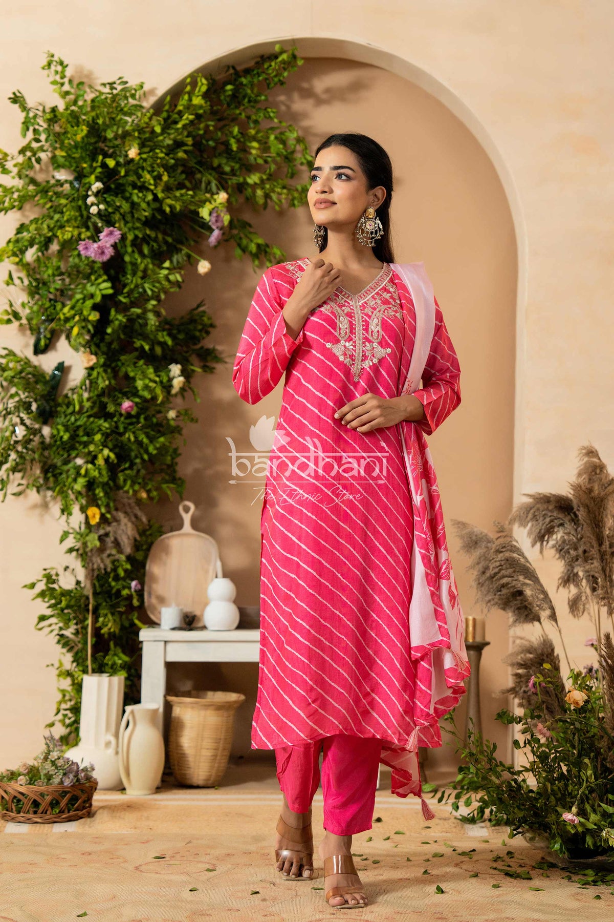 Woman in a pink traditional outfit standing in a decorated indoor setting with plants and decor.