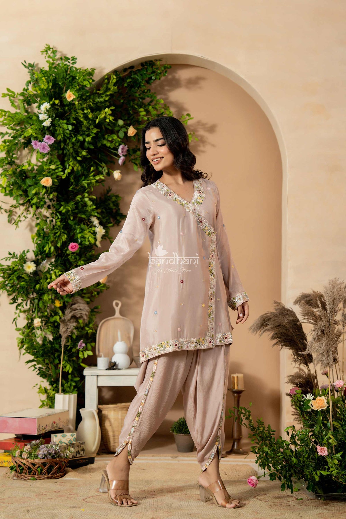 Woman in a traditional outfit standing in a decorated room with plants and flowers.