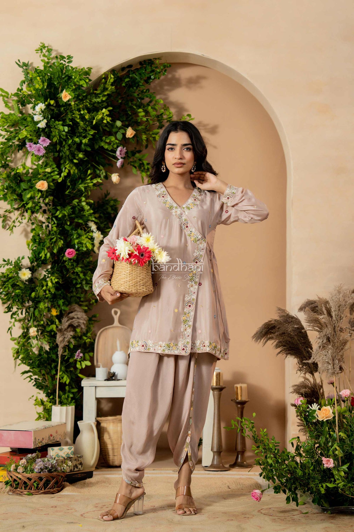 Woman in a floral outfit standing in a decorated room with plants and flowers.