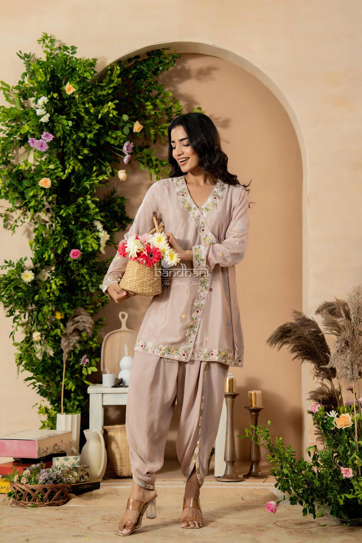 Woman in a light pink traditional outfit holding flowers in a decorated indoor setting.
