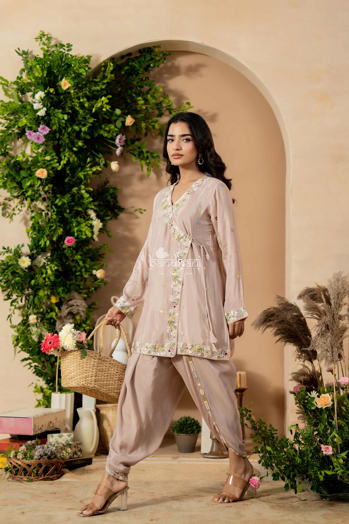 Woman in a light pink traditional outfit standing in front of floral decorations.