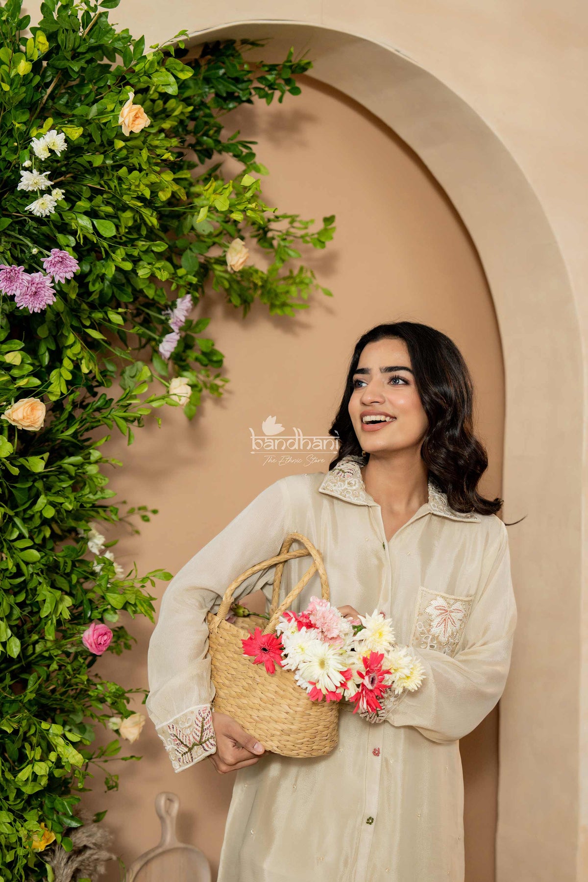 Woman holding a basket of flowers against a decorative wall with plants