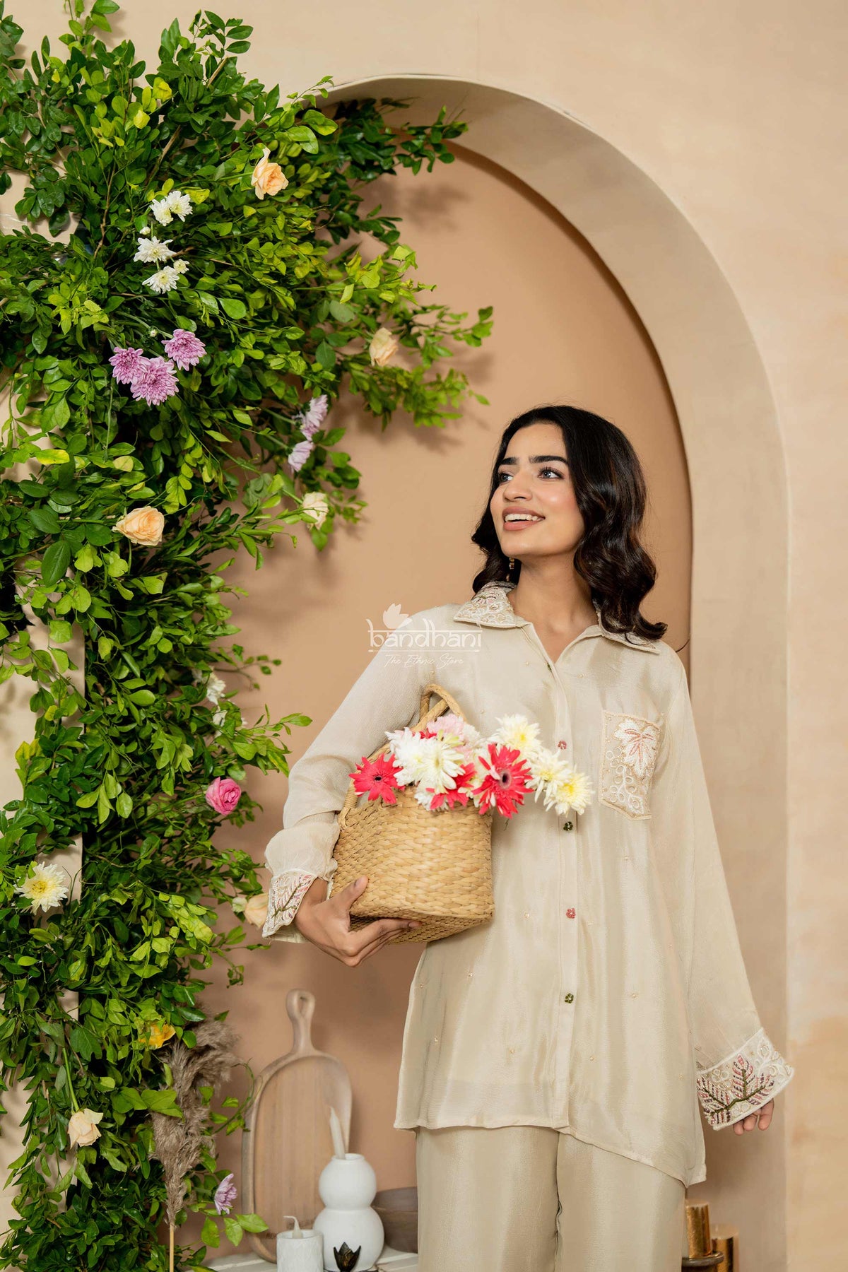 Woman holding a basket of flowers in a decorated indoor setting with greenery and archway.