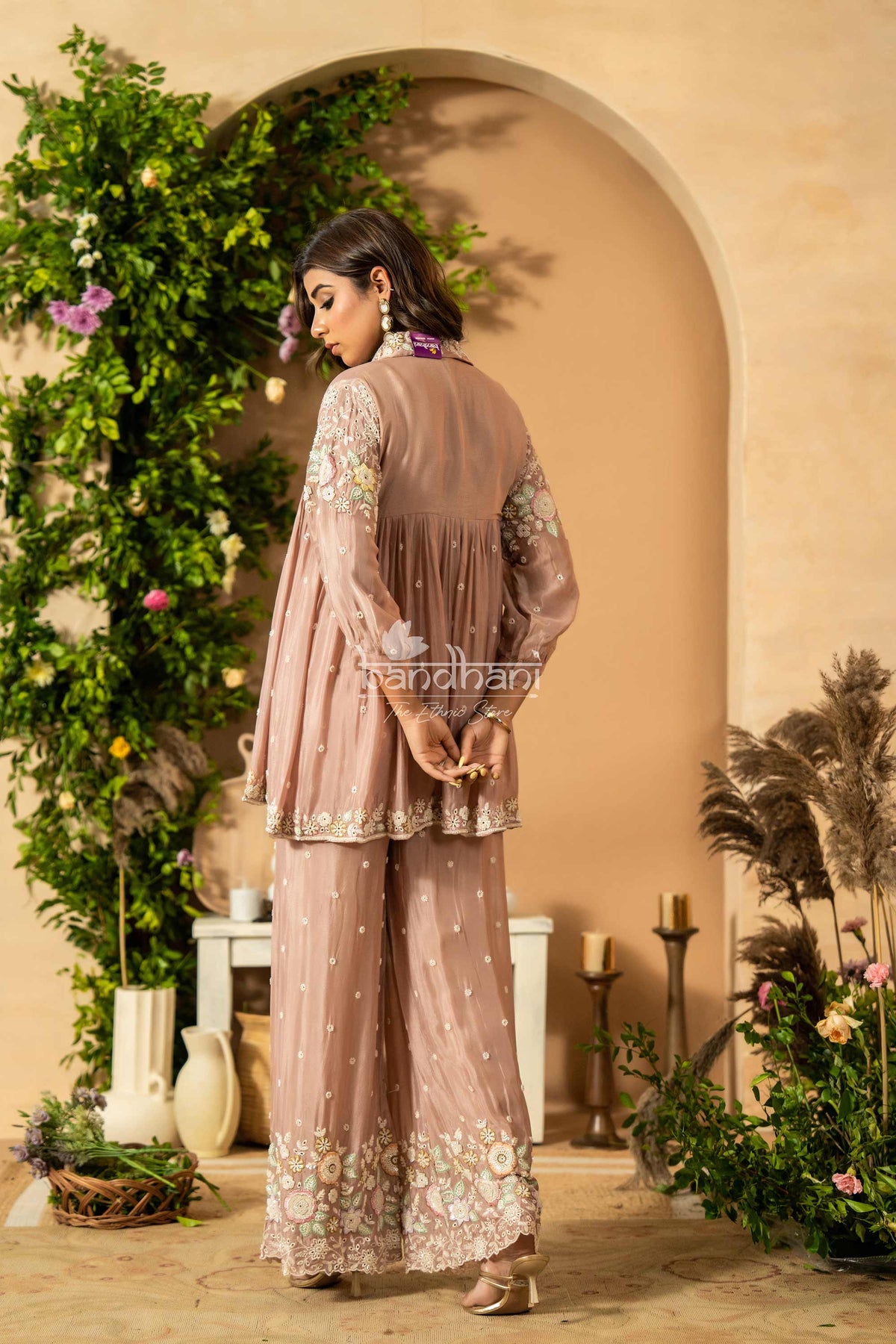 Woman in a pink traditional outfit standing in front of an archway with decorative plants and candles.