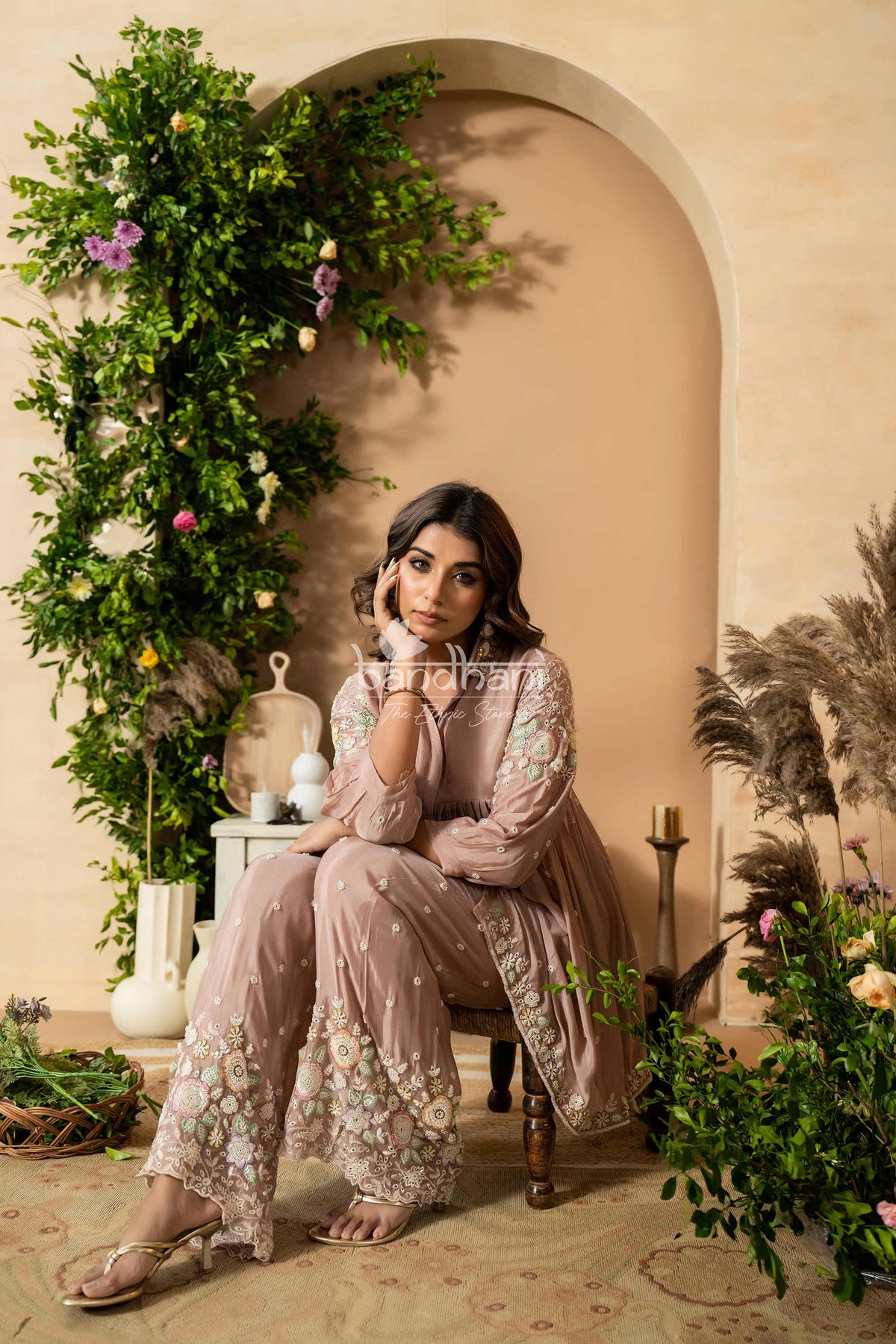 Woman in a floral outfit sitting in a decorated room with plants and candles.