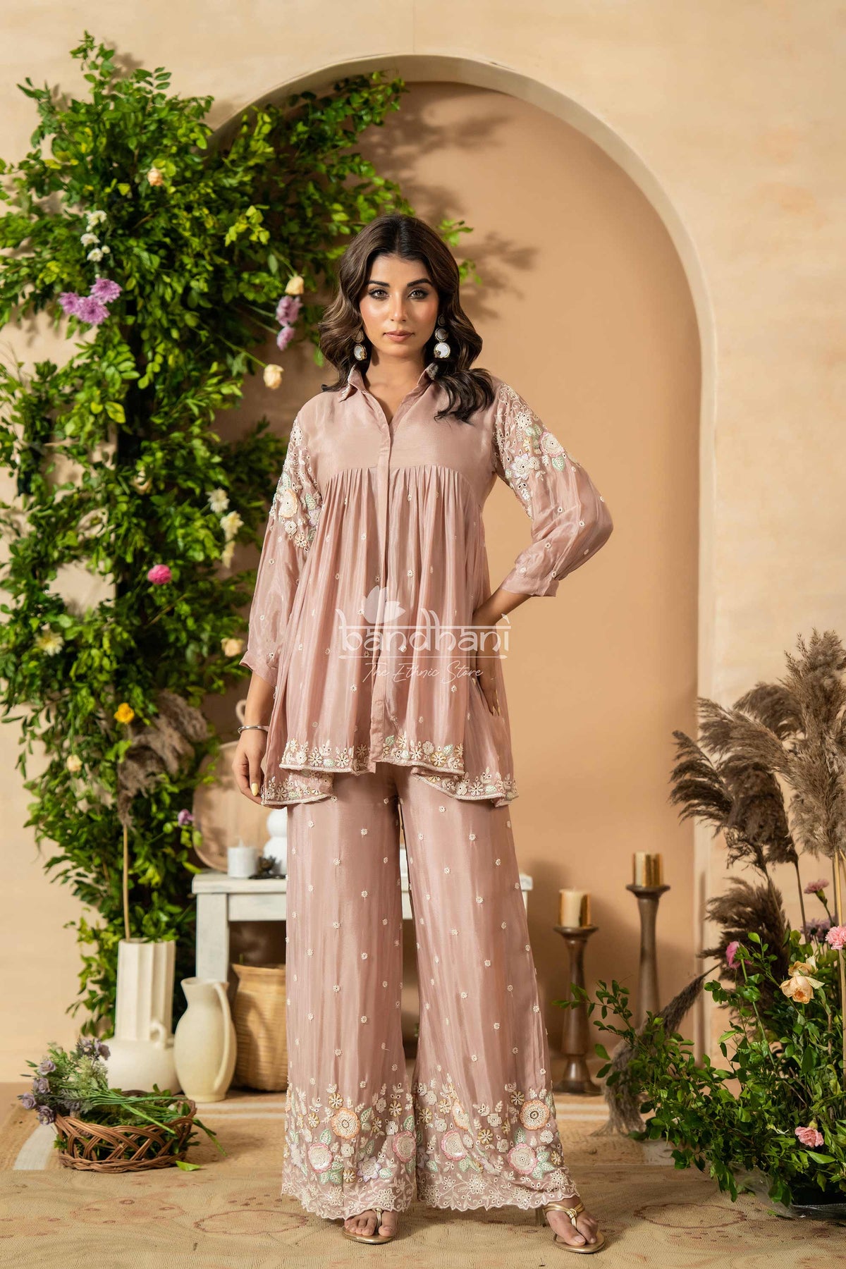Woman in a pink traditional outfit standing in front of an archway with decorative plants.