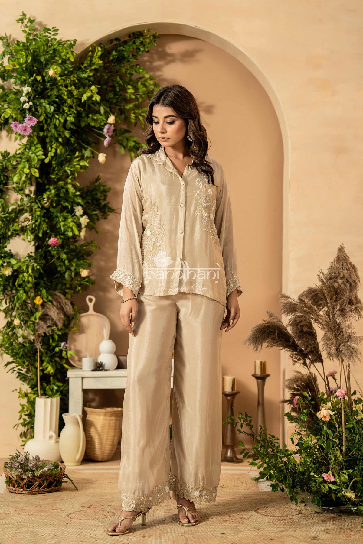 Woman in a beige outfit standing in a decorated indoor setting with plants and decor.