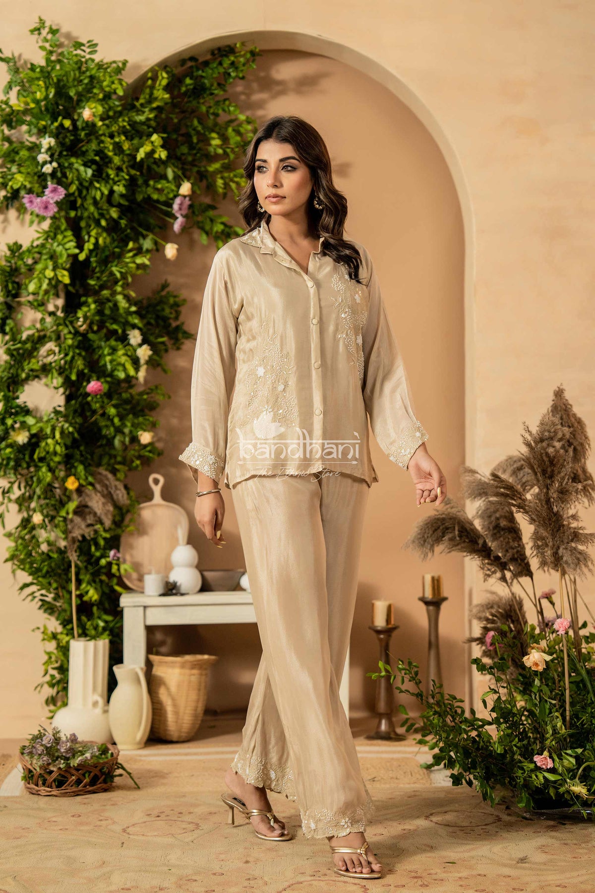 Woman in a beige outfit standing in a decorated room with plants and decor.