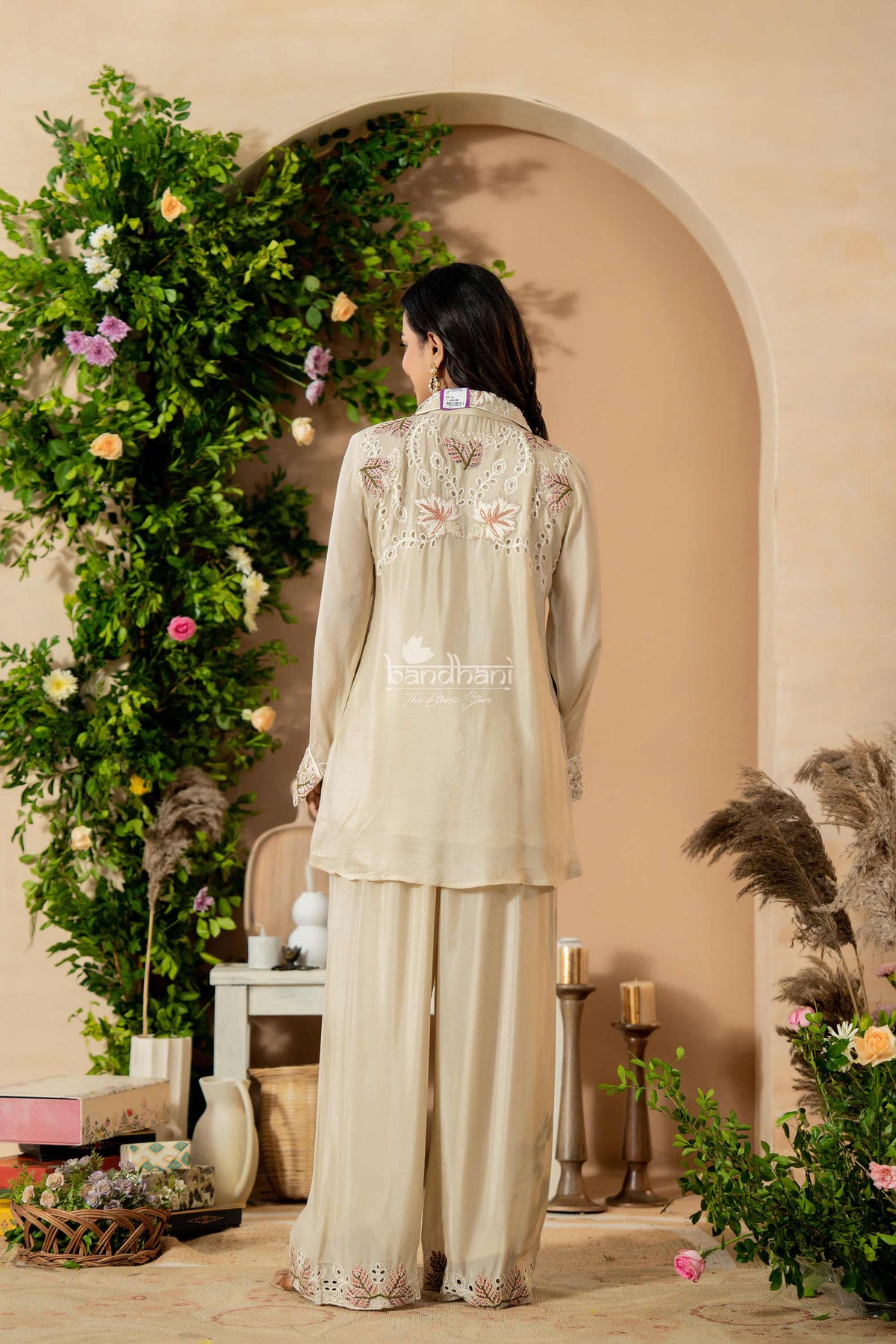 Woman in a cream embroidered outfit standing in a decorated room with flowers and candles.