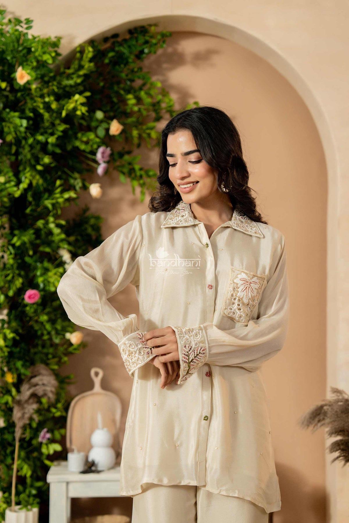 Woman wearing a light-colored outfit with lace details in an indoor setting with greenery.