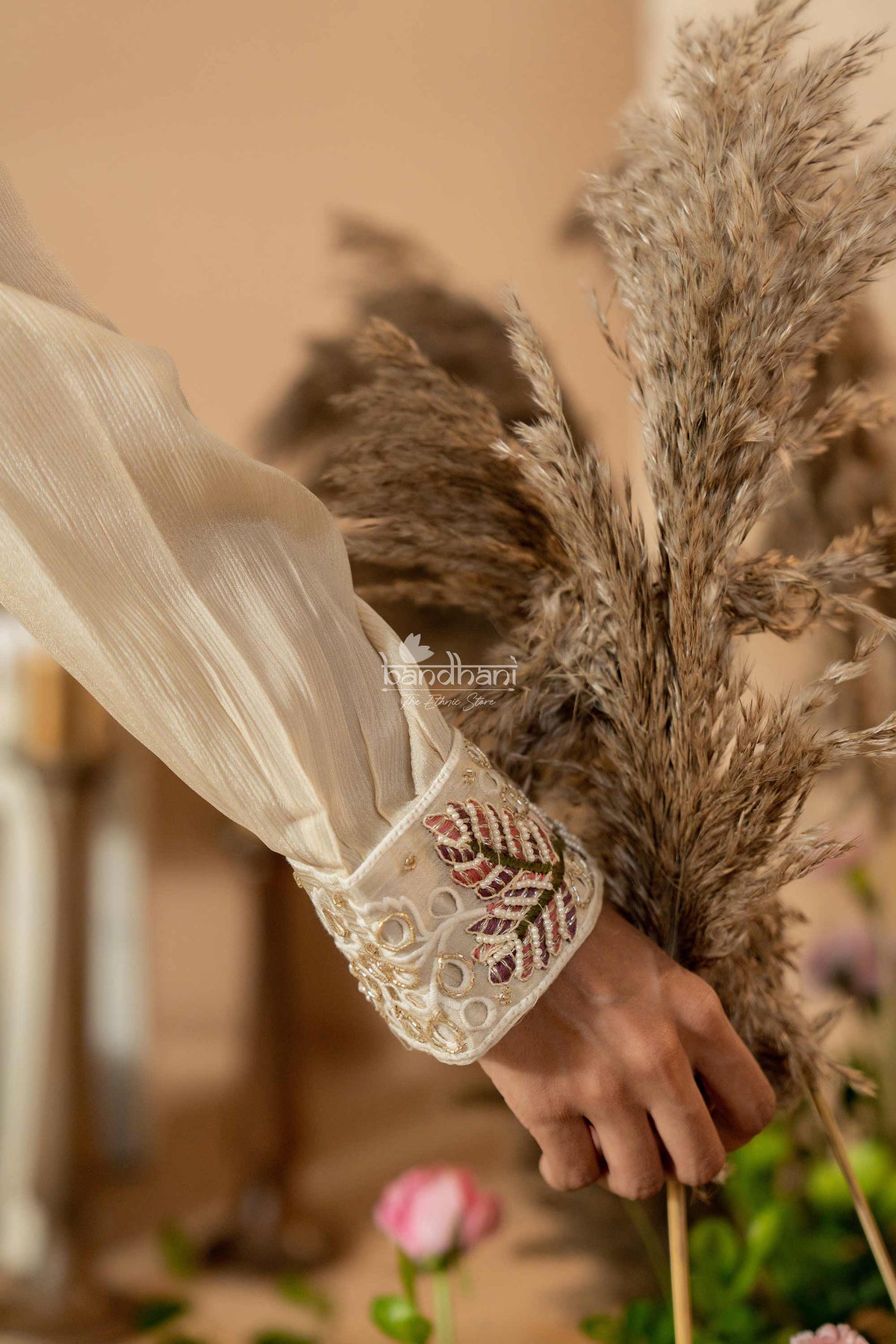 Hand holding dried pampas grass with embroidered sleeve in the foreground