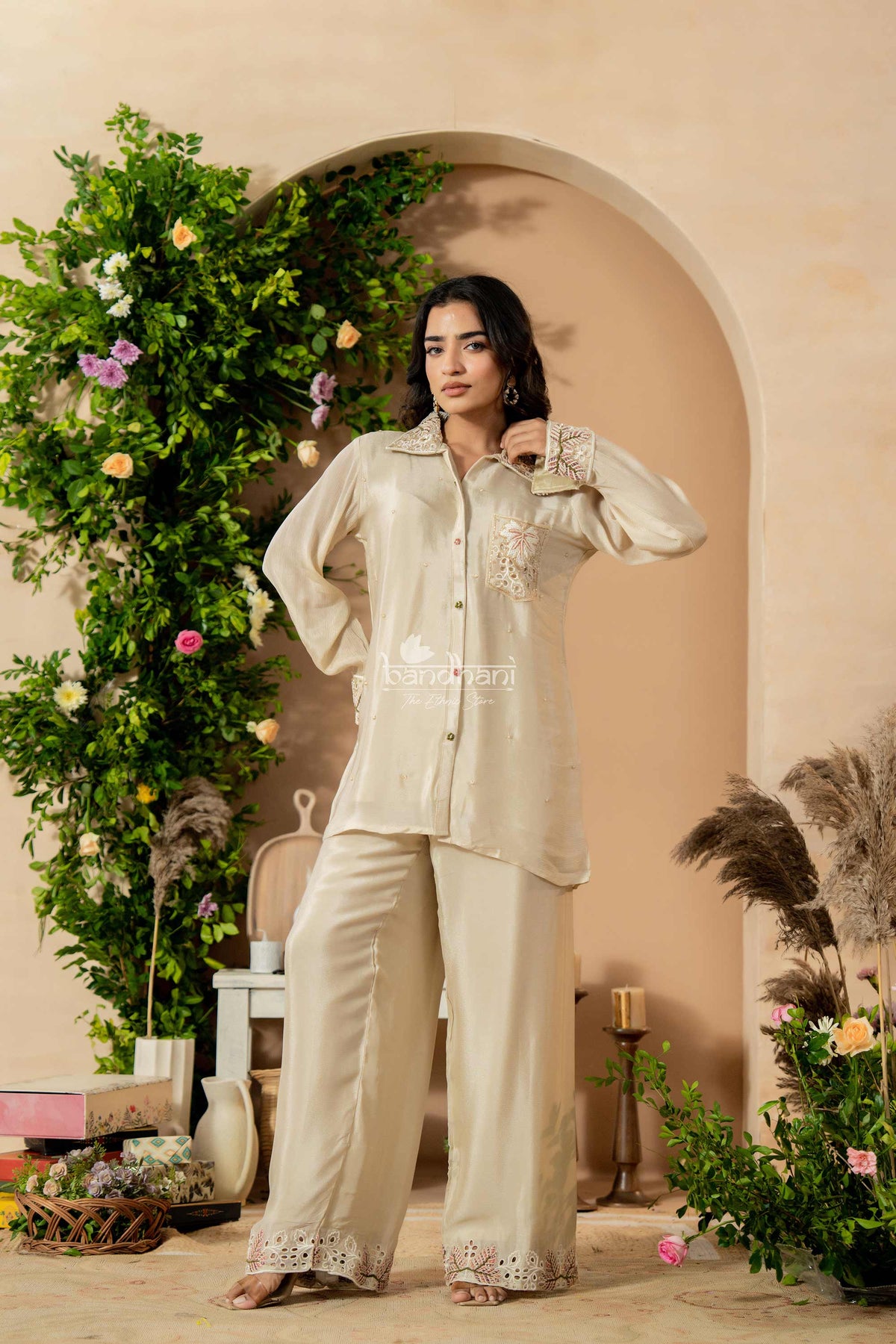 Woman in a light-colored outfit standing in a decorated room with plants and flowers.