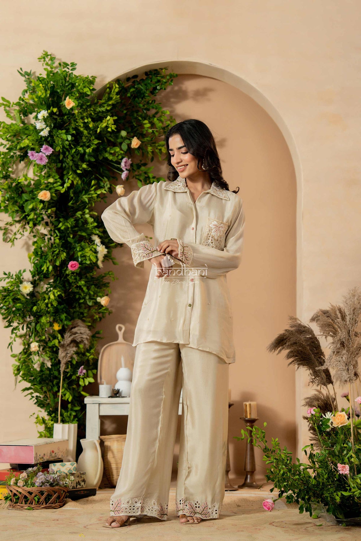 Woman in a beige outfit standing in a decorated room with flowers and decor.