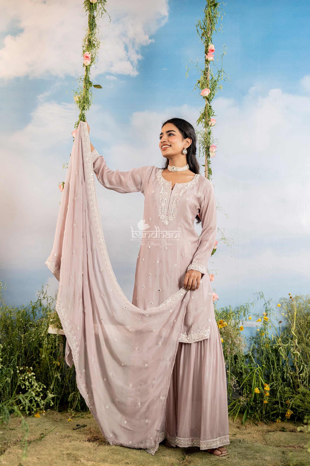 Woman in a light pink traditional outfit standing outdoors with a scenic background