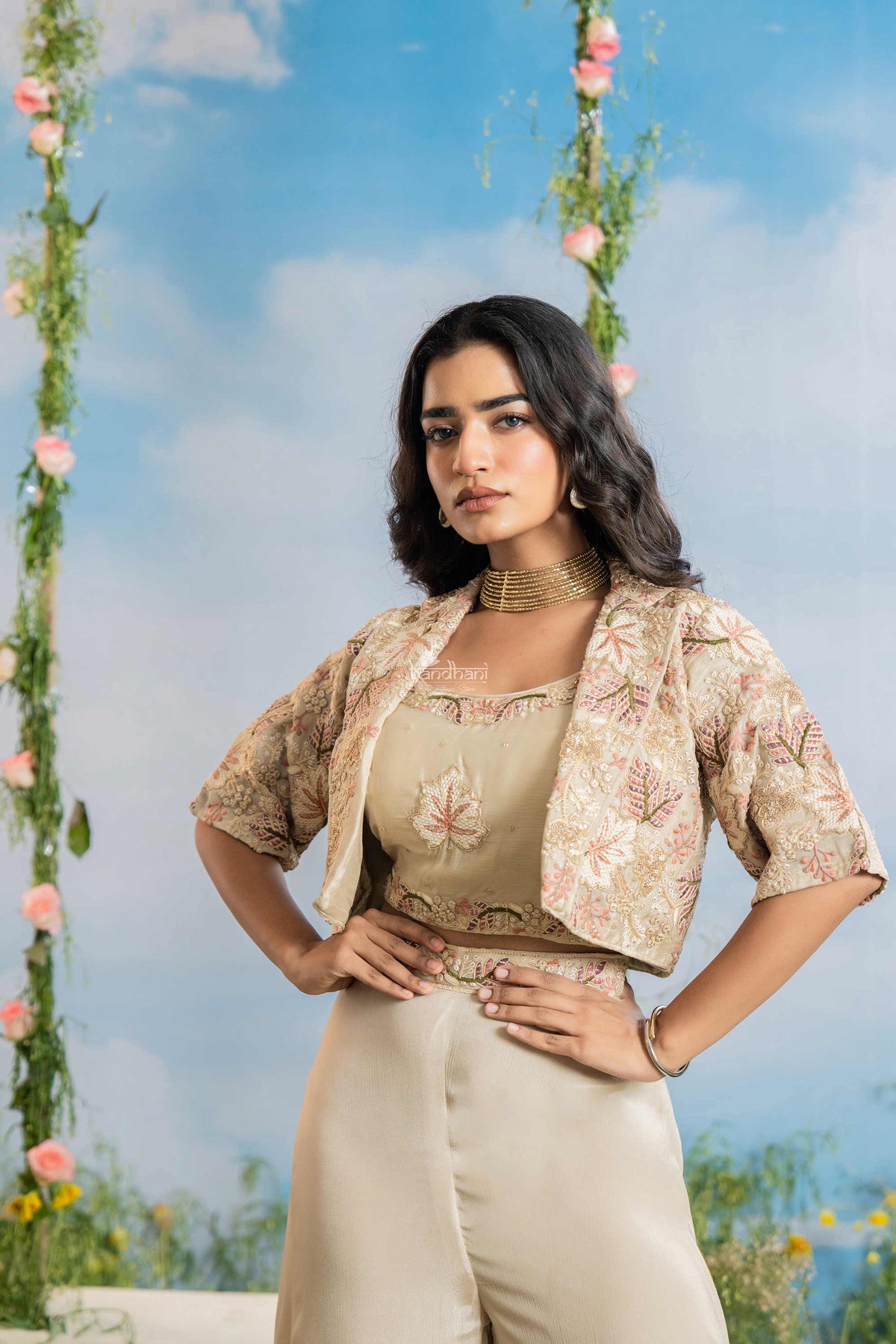 Woman in a floral top and beige pants standing against a blue sky with floral decorations.
