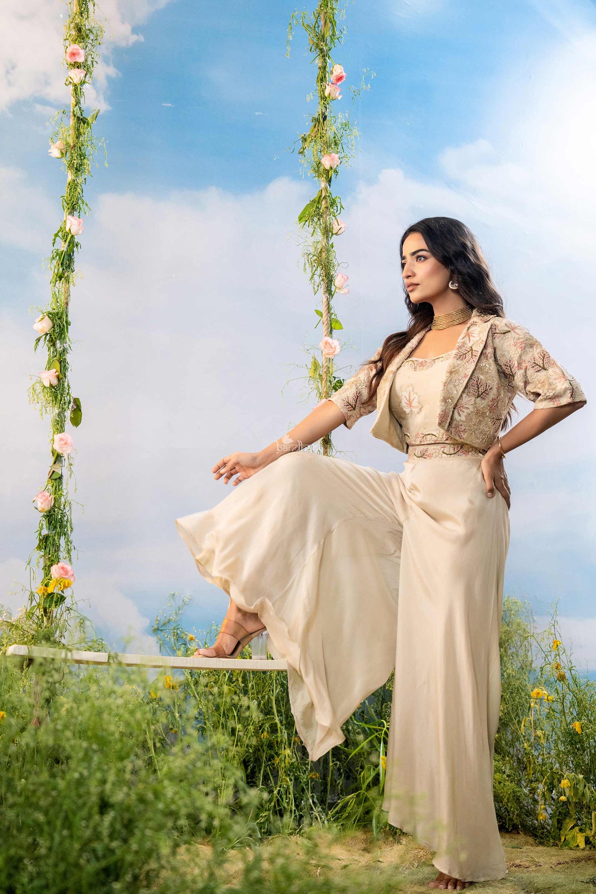 Woman in a beige outfit sitting on a swing with floral decorations against a blue sky.