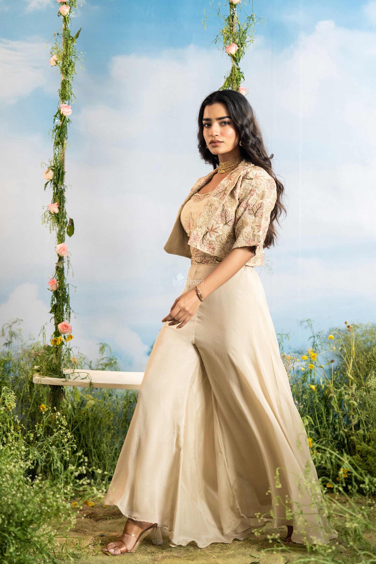 Woman in a beige outfit sitting on a swing with floral decorations against a blue sky.