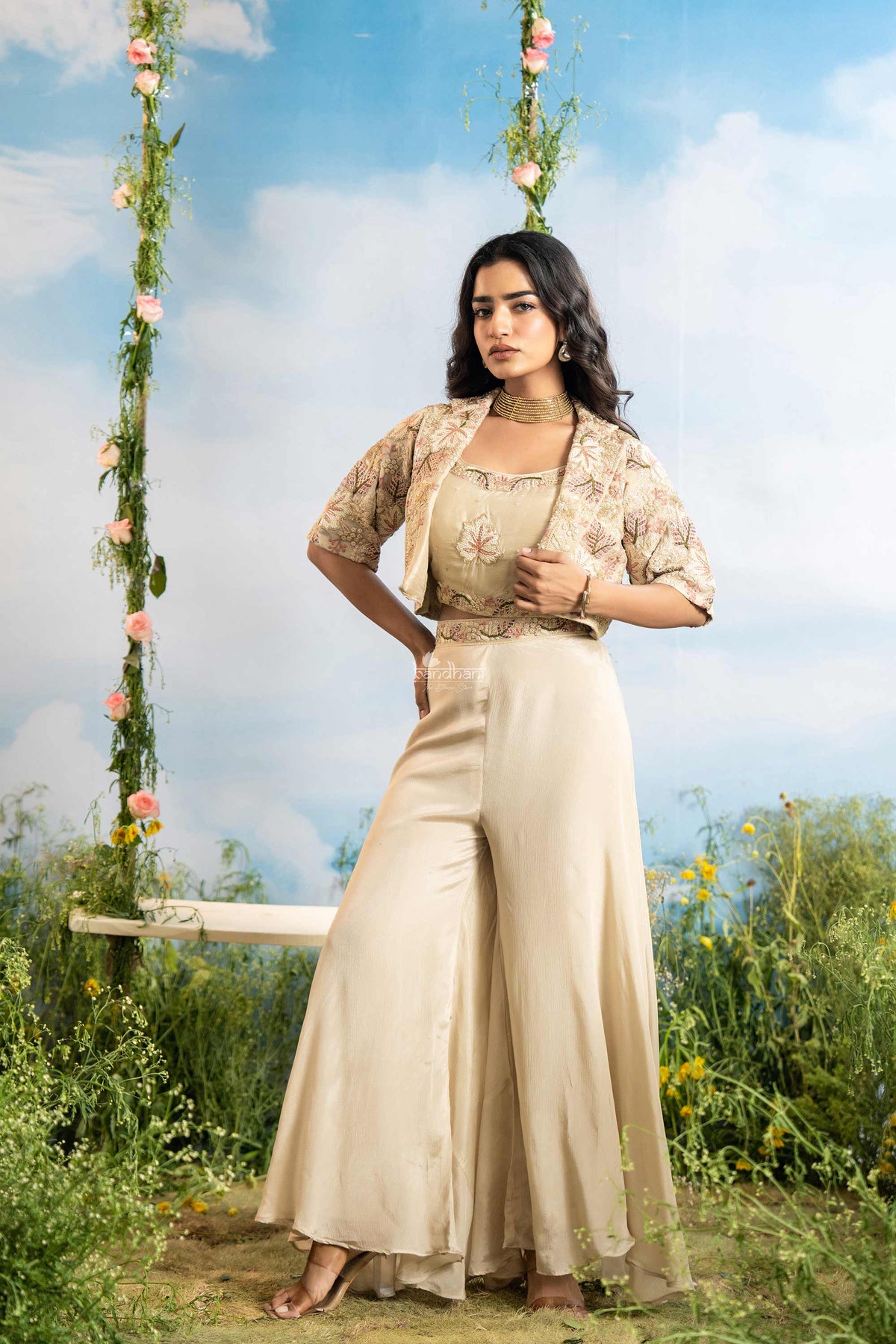 Woman in a beige outfit sitting on a swing with floral decorations against a blue sky.