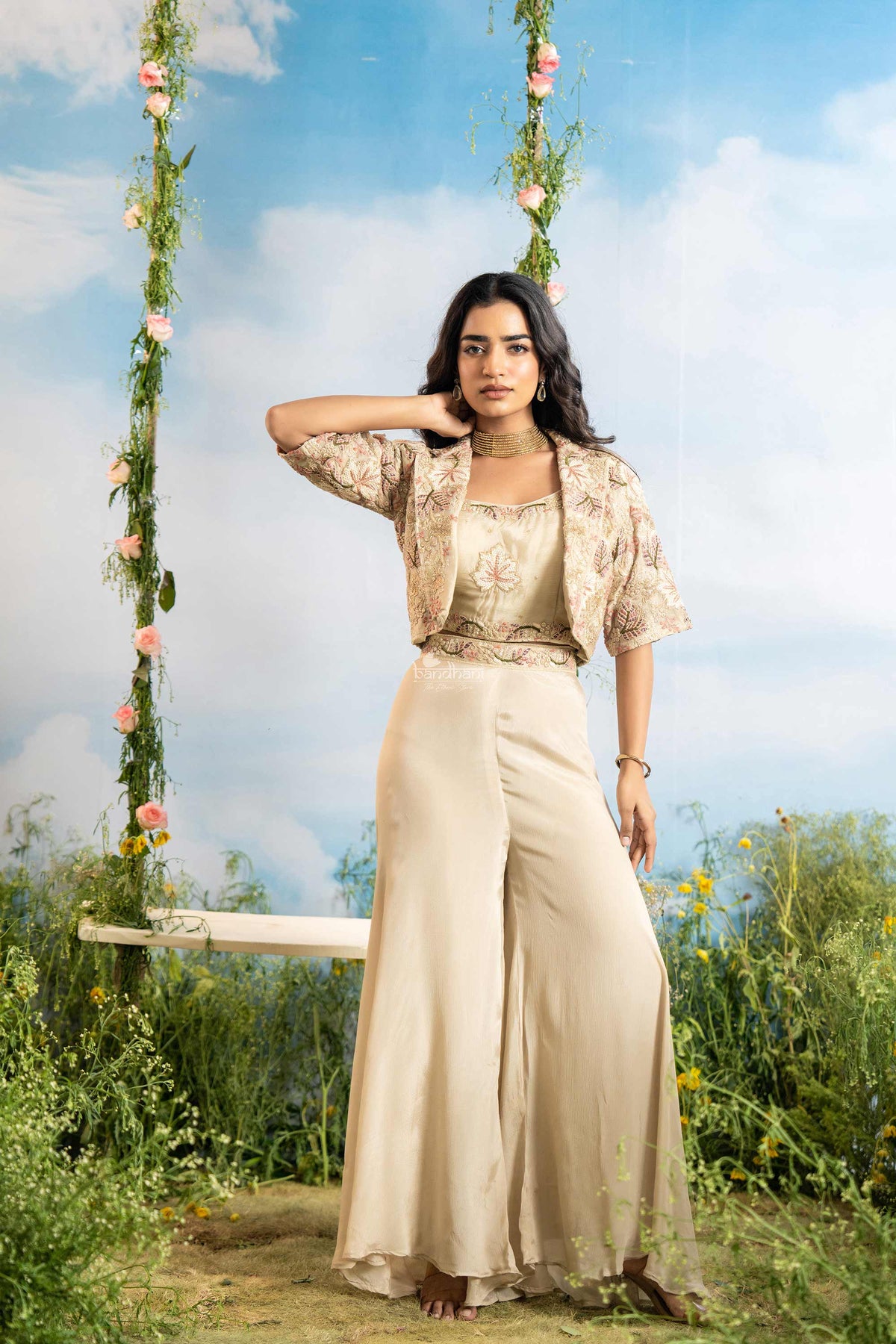 Woman in a beige outfit standing next to a floral swing with a blue sky background