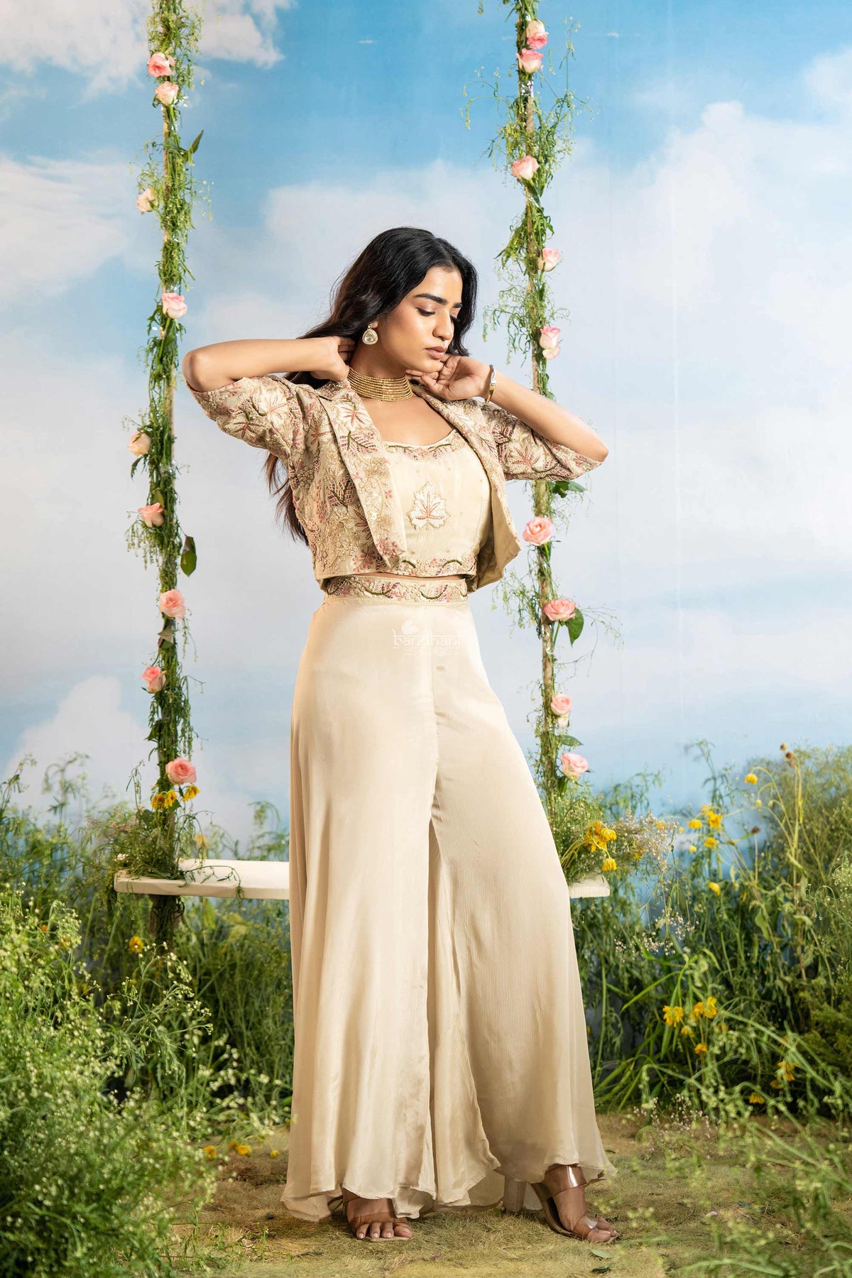 Woman in a beige outfit sitting on a swing with floral decorations against a blue sky.