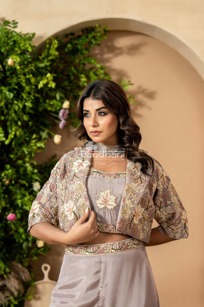 Woman wearing a floral blouse and light-colored pants against a beige wall with greenery.