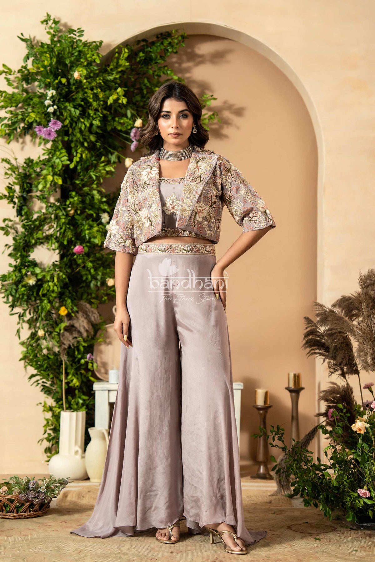 Woman in a stylish outfit standing in an elegant indoor setting with decorative plants and archway.