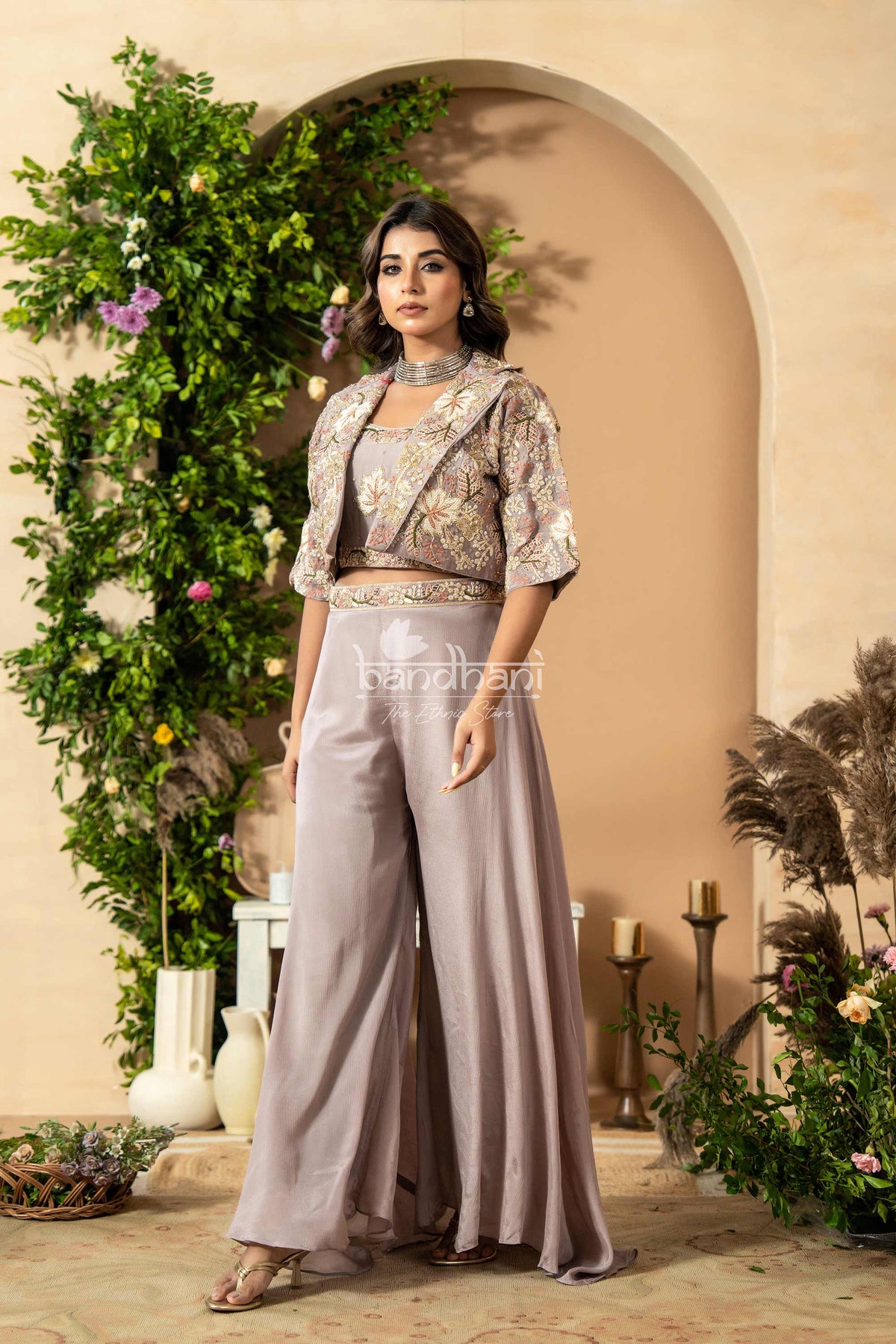 Woman in a stylish outfit standing in an elegant indoor setting with floral decorations.